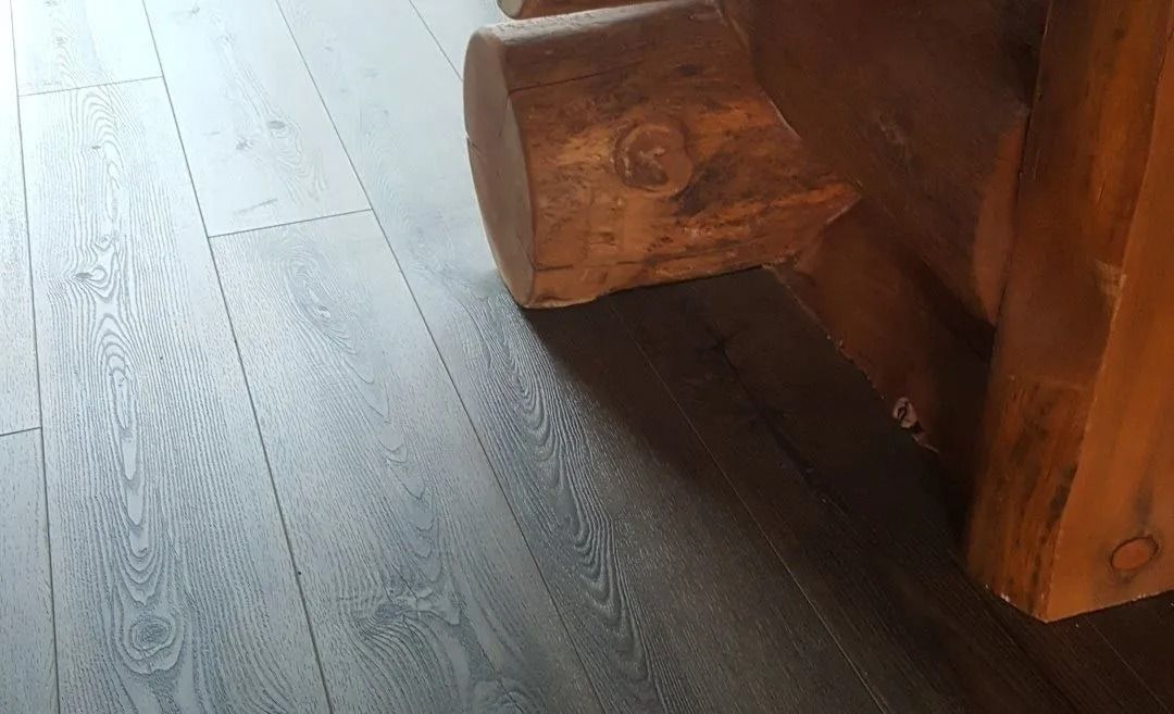 Close-up of a wooden furniture leg on a dark wood floor with sunlight streaks.