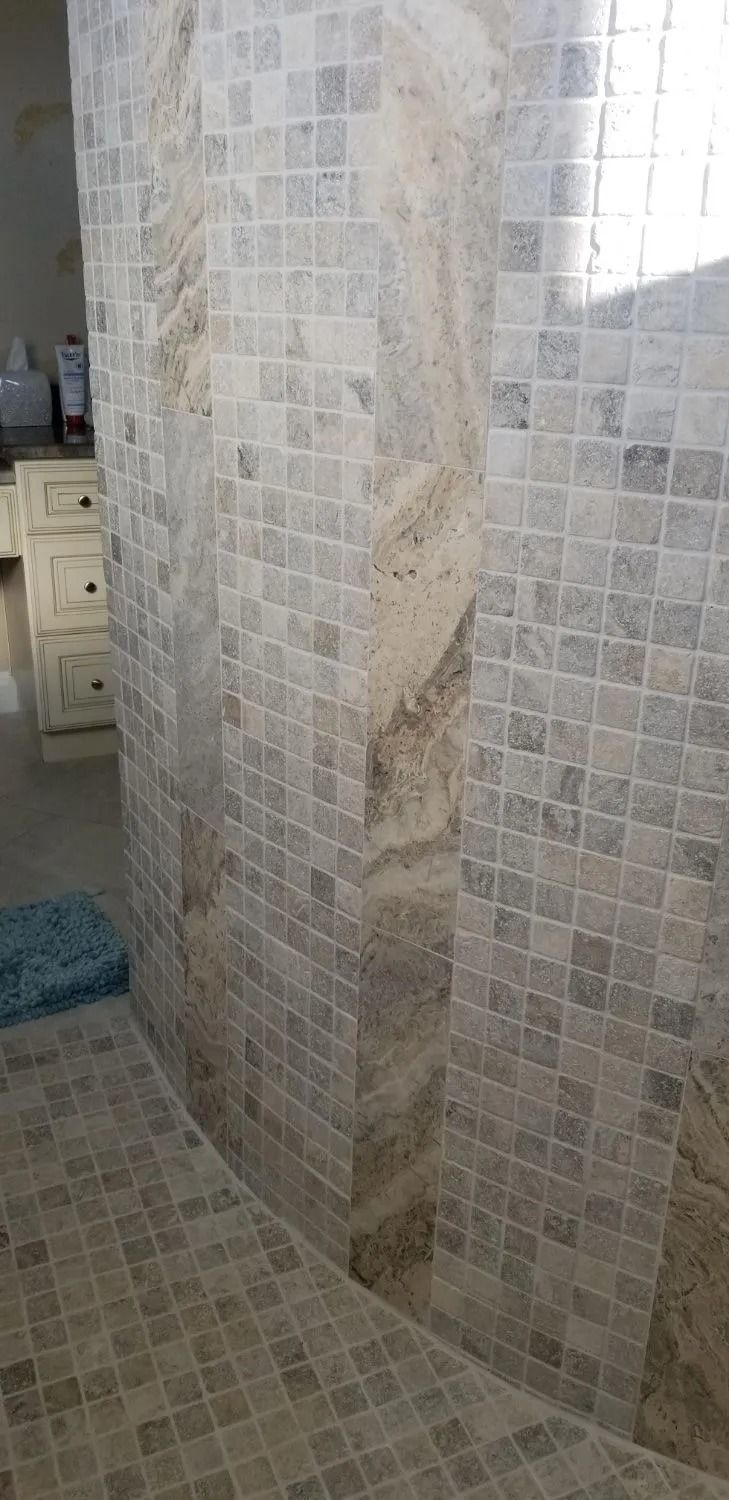 Tiled shower corner with beige mosaic walls and floor, showing a built-in niche and bench seat