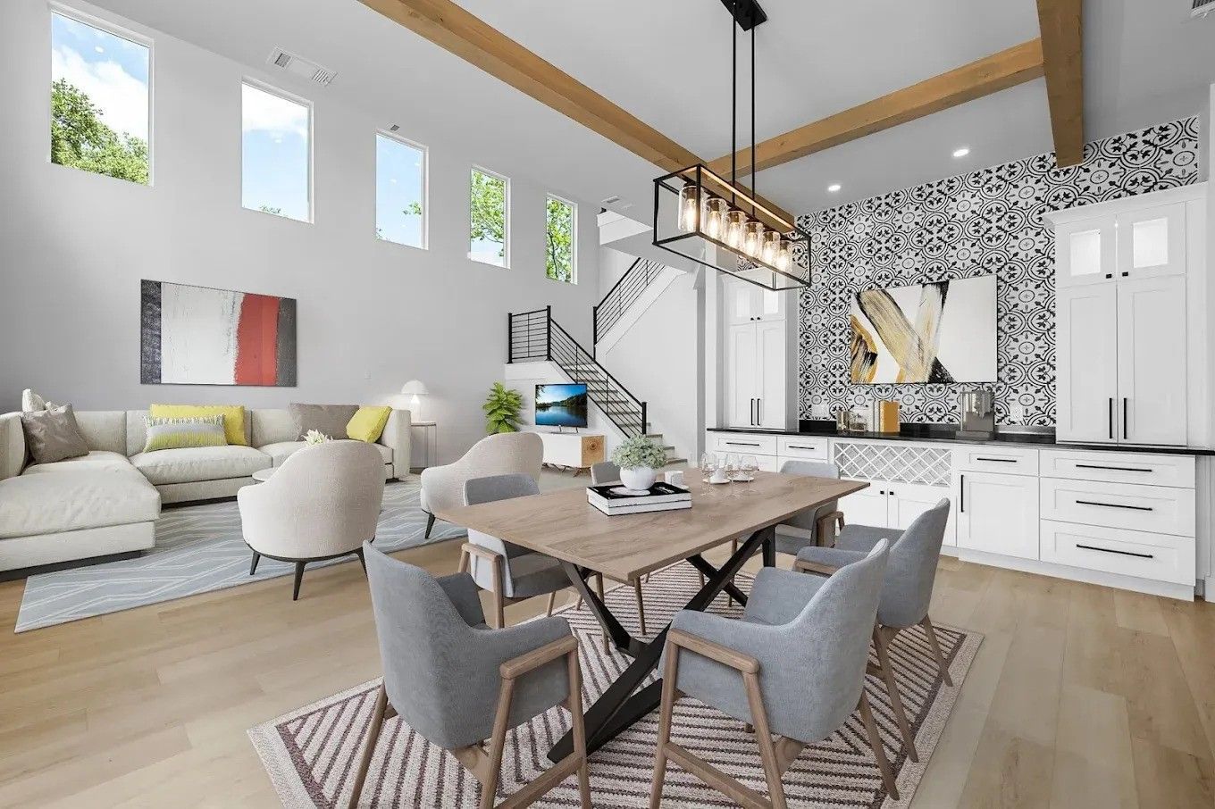 Bright open-plan living room and dining area with white sofas, wooden table, staircase, and black-and-white kitchen
