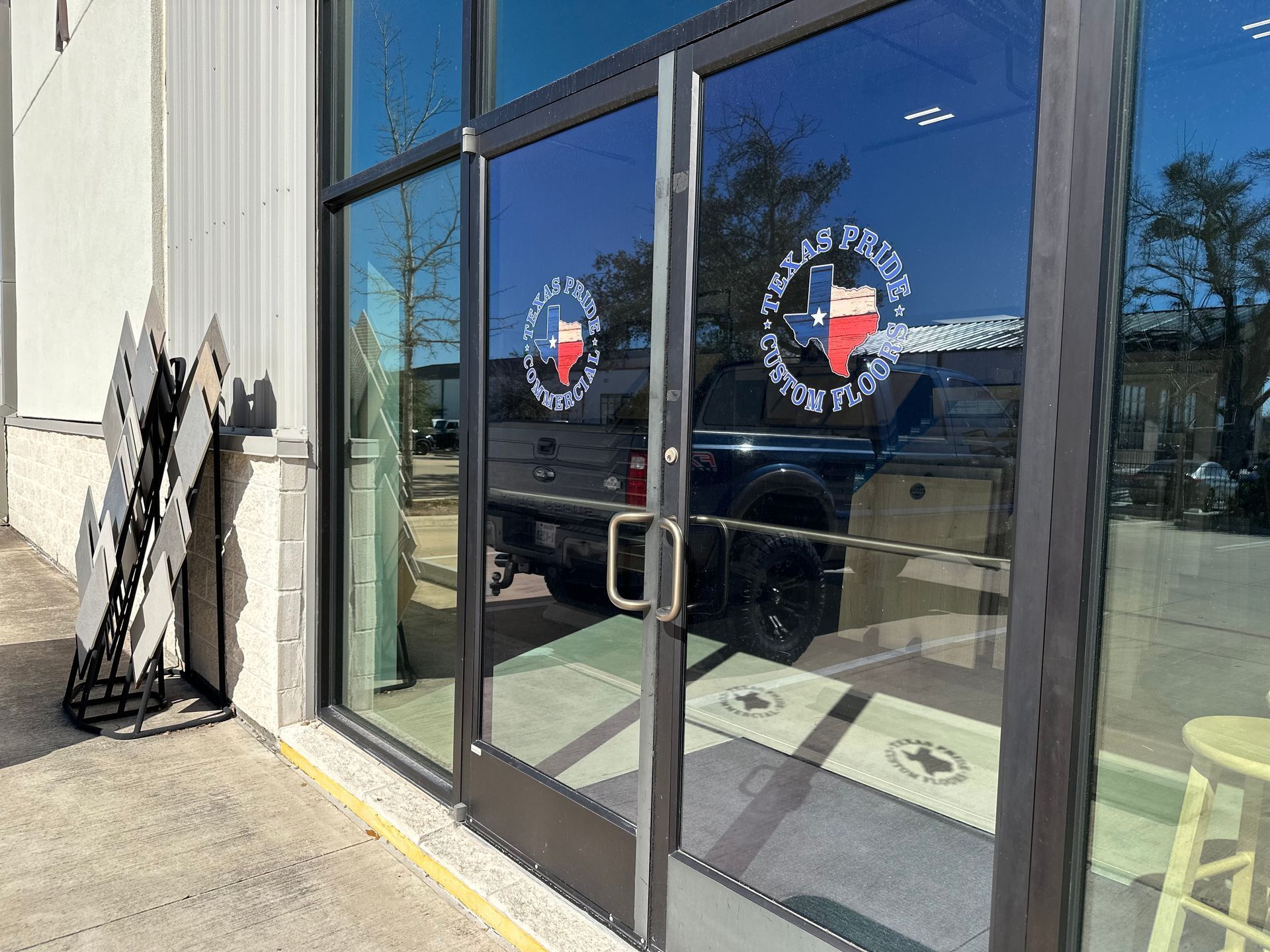 Glass storefront entrance with double doors, reflections, and a yellow wheelchair ramp curb.