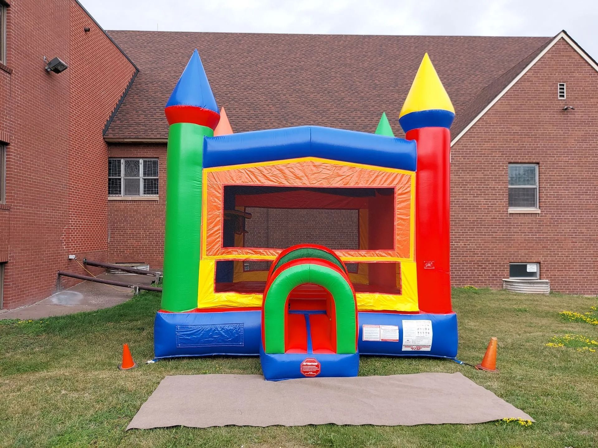 Colorful inflatable bounce house with red, blue, green, and yellow accents sits on grass in front of a brick building.
