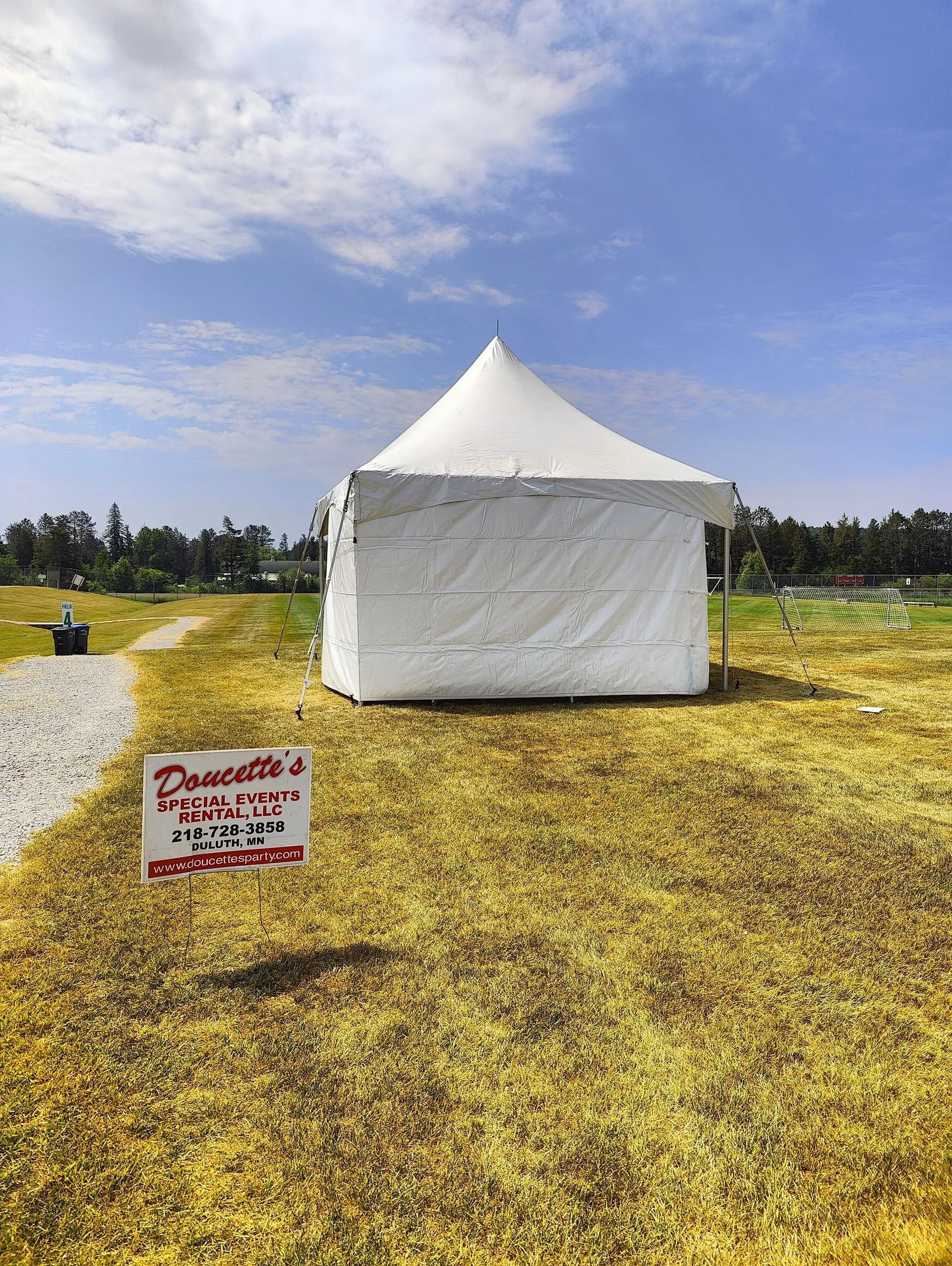 White tent on a grassy field, a sign in front reads