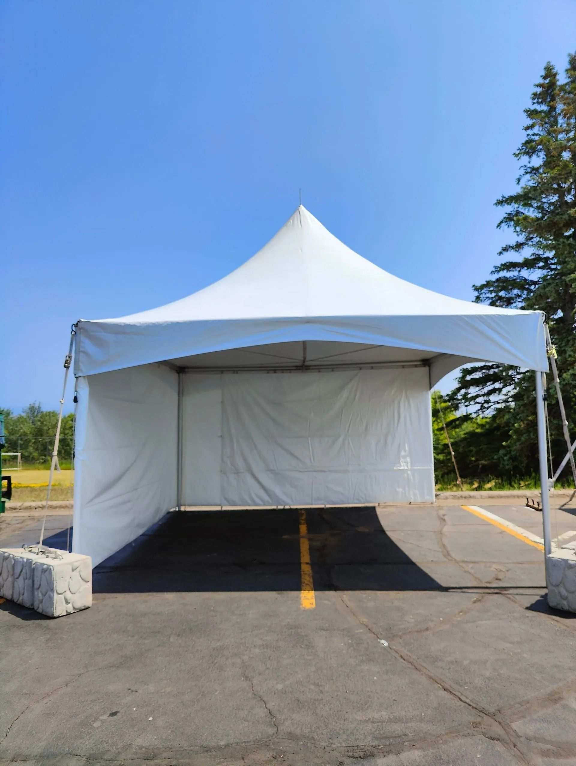White tent set up on asphalt, with a clear blue sky.