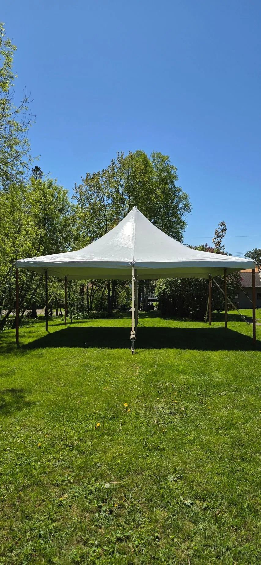 A white canopy tent set up on green grass with trees in the background under a blue sky.