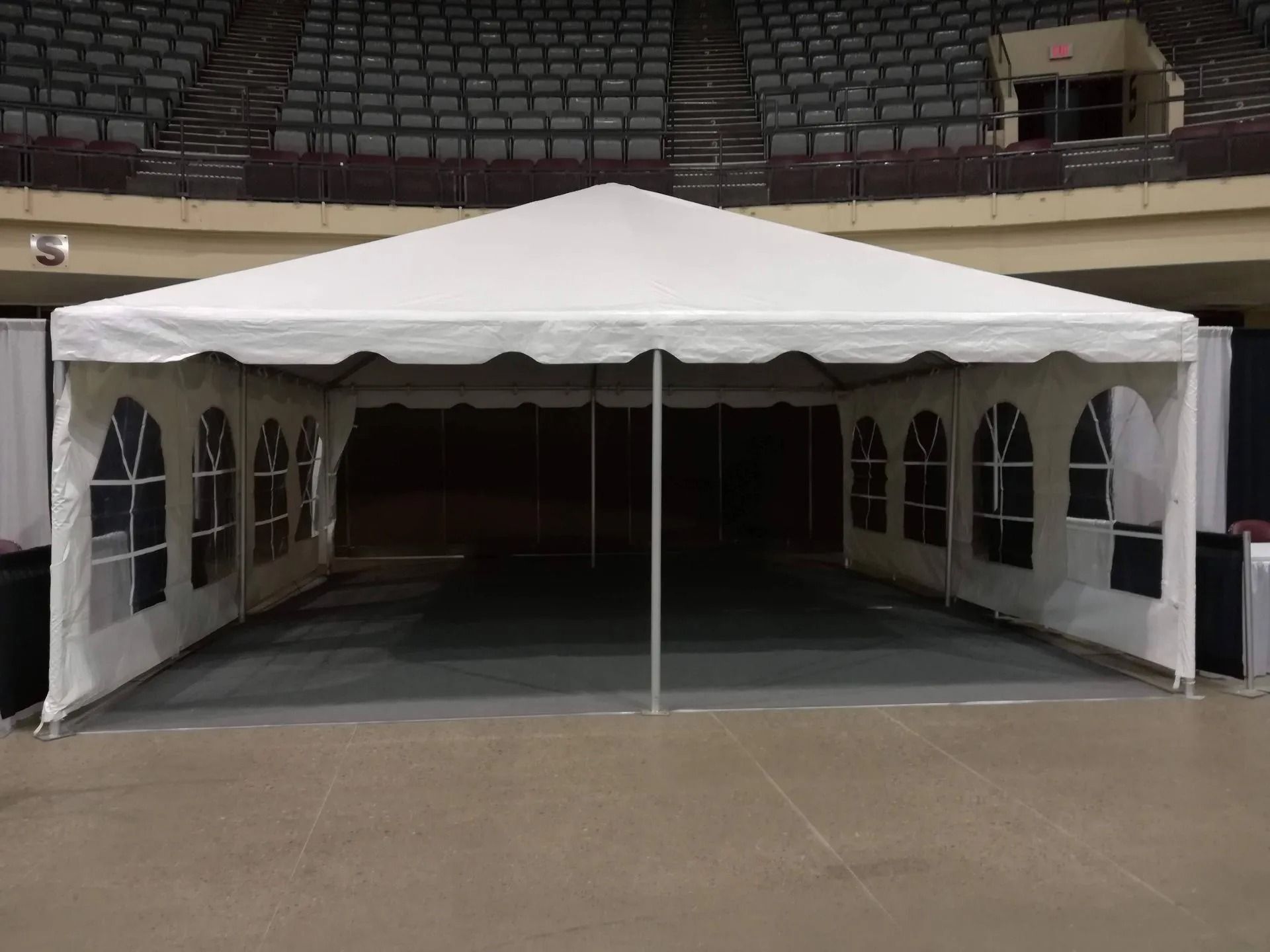 White tent set up inside an arena. The tent has windows and a center support pole.