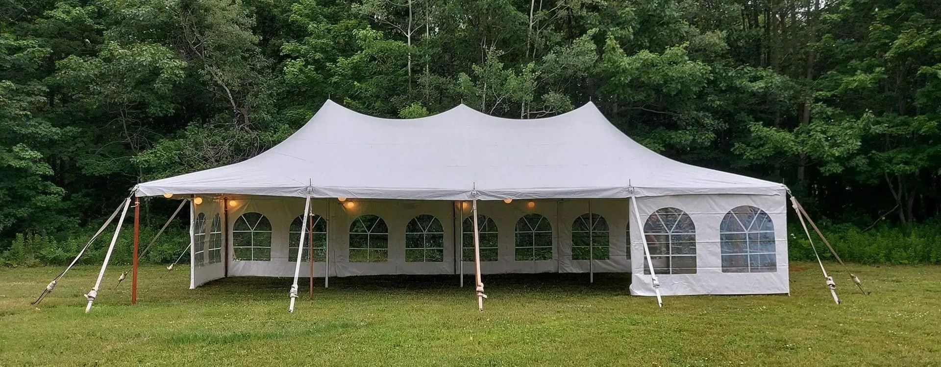White tent set up on a grassy field with a forest background.