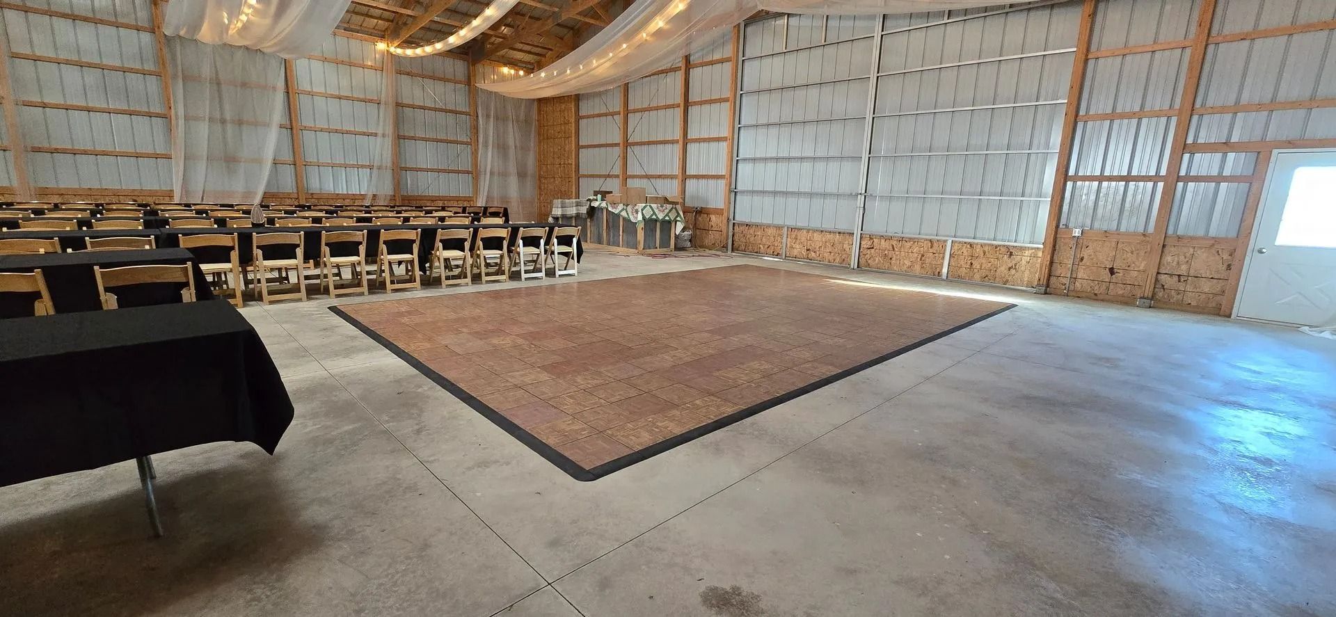 Empty event space with rows of chairs, a dance floor, and a draped table.