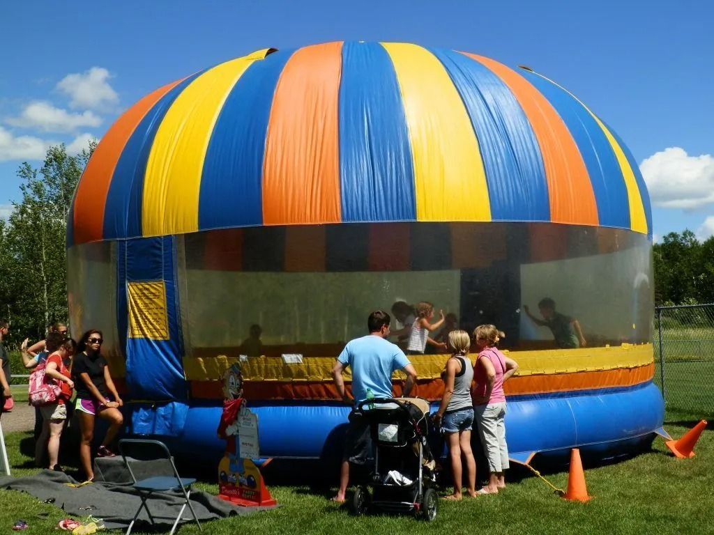 Large, colorful inflatable bounce house in a park; children inside, adults watching.