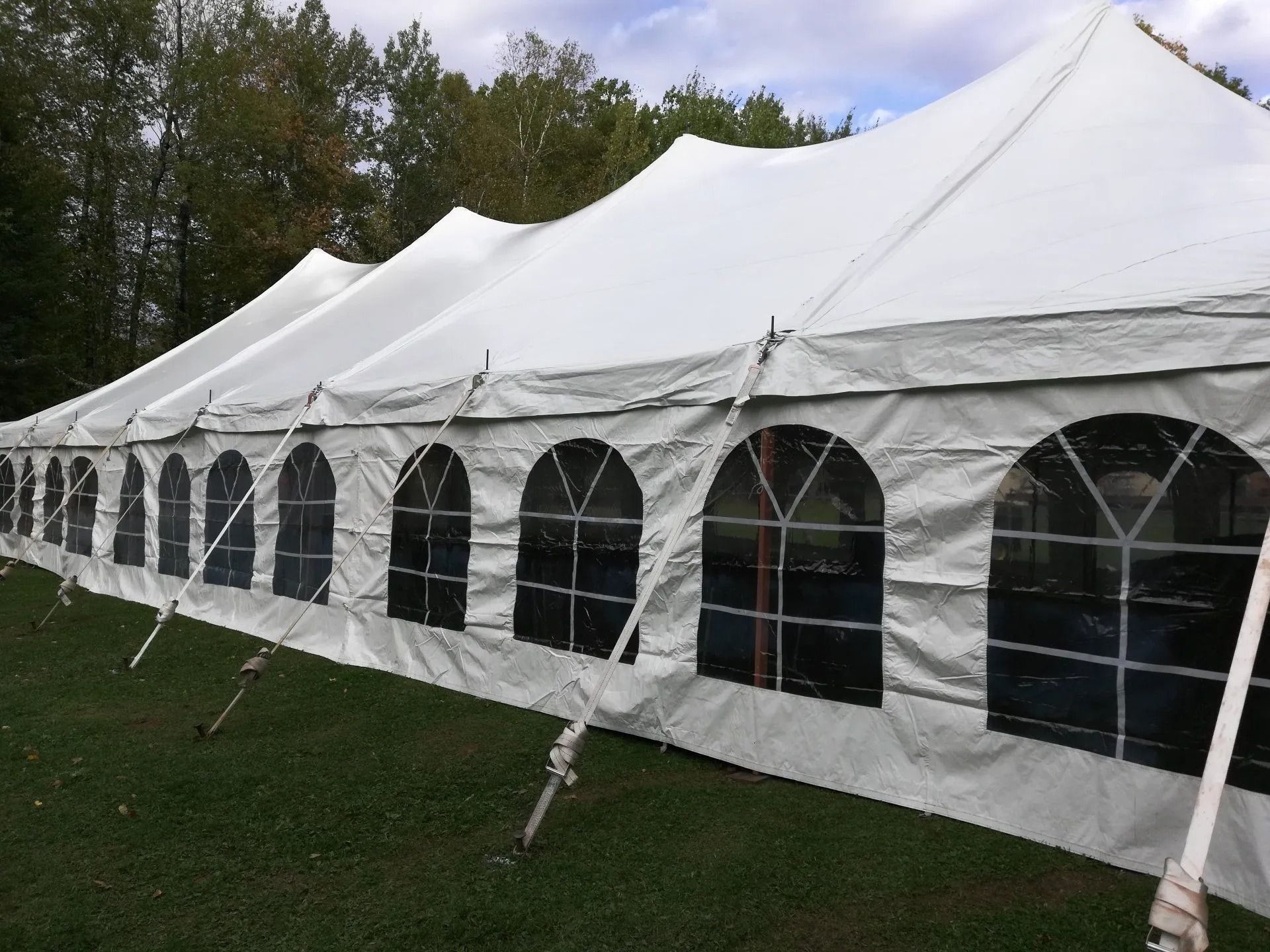 White tent with arched windows set up on green grass. Trees in the background.