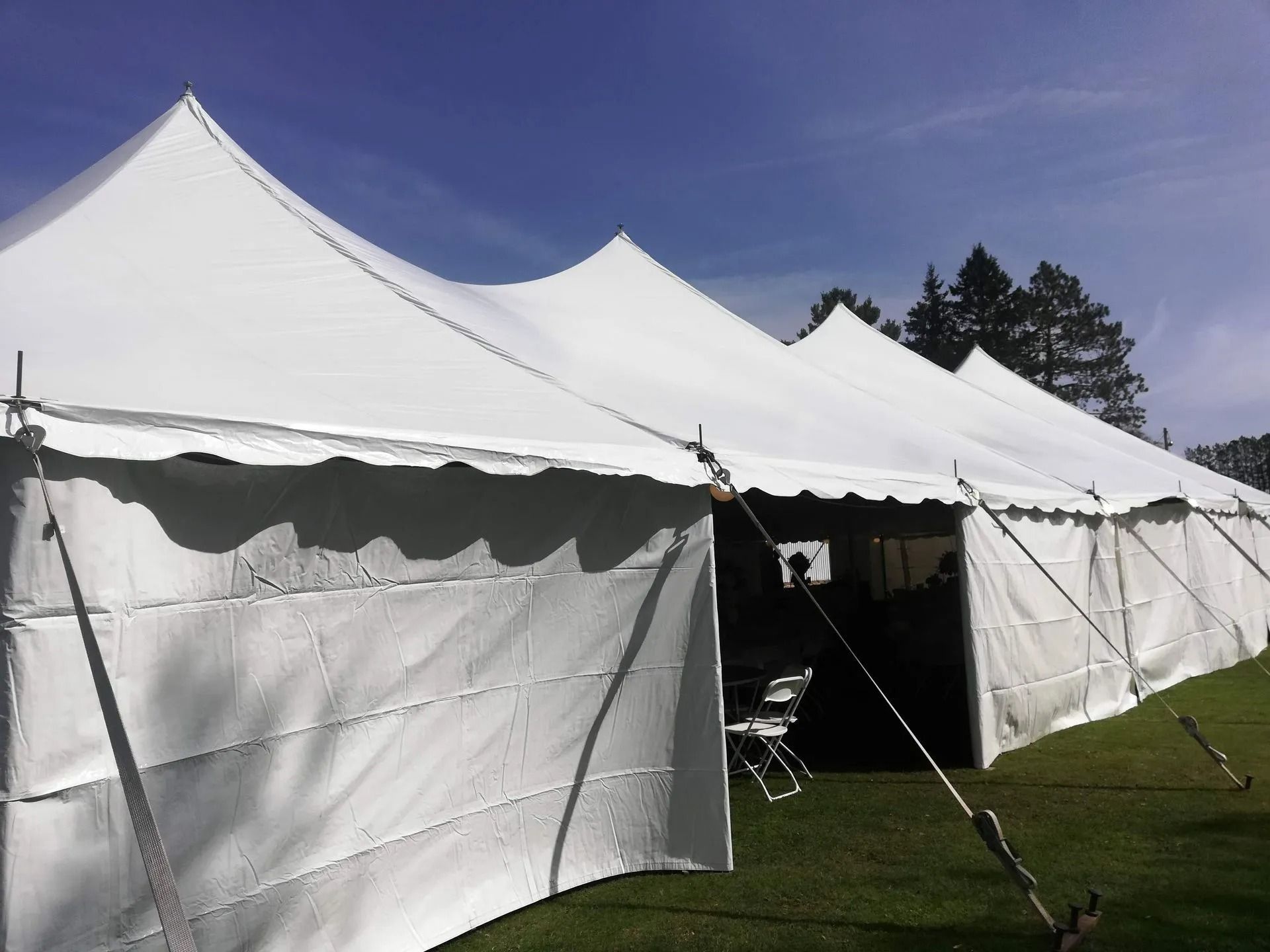 White party tent on green grass under a blue sky, with trees in the background.