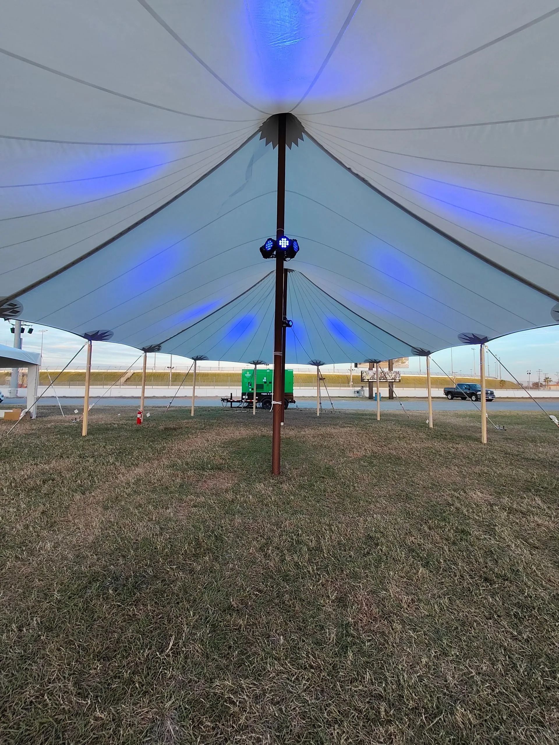 Inside a tent, lights shine on the white fabric roof. Grass is visible below.