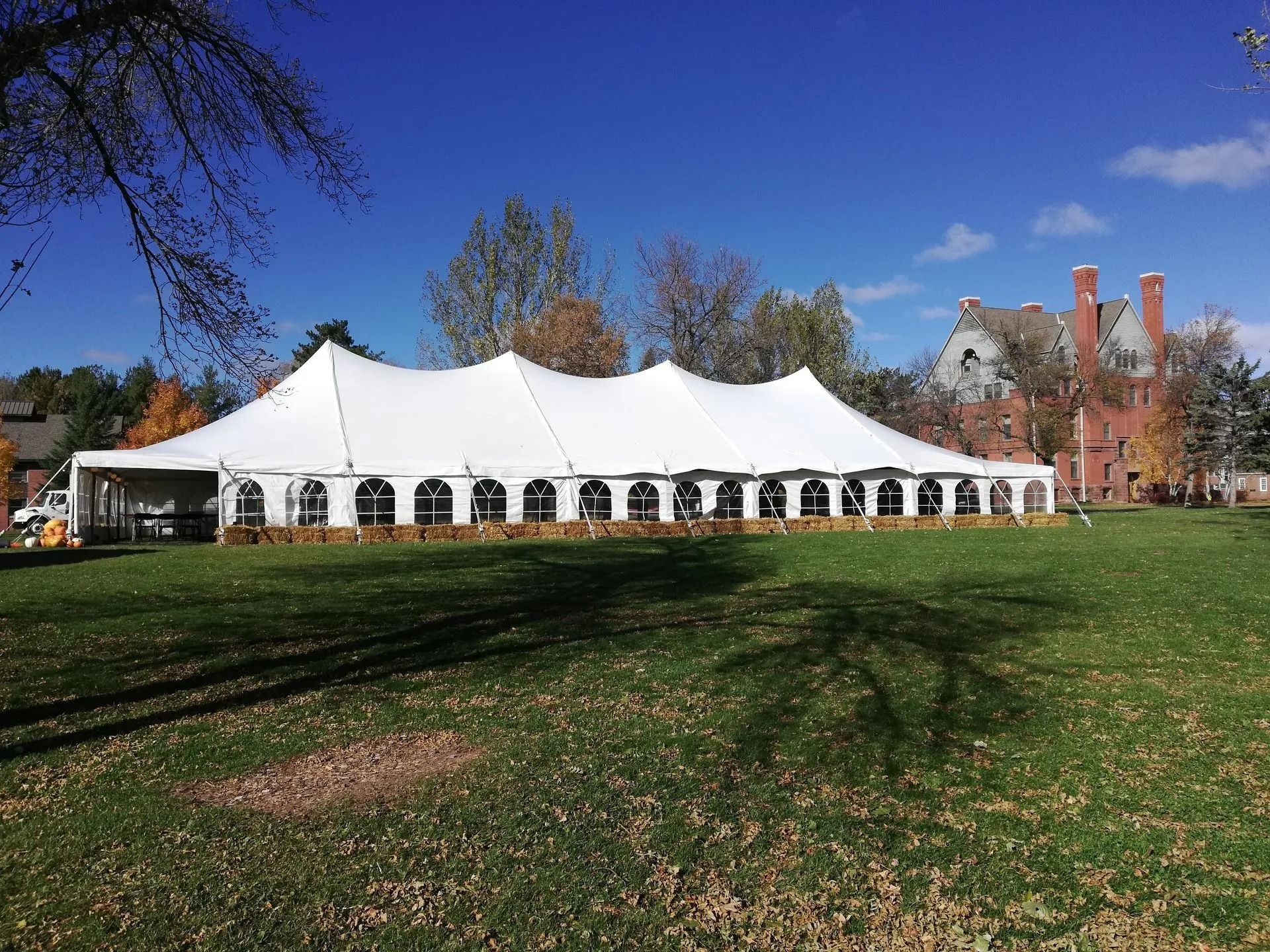 White tent set up on a grassy lawn with a building in the background. Bright blue sky overhead.