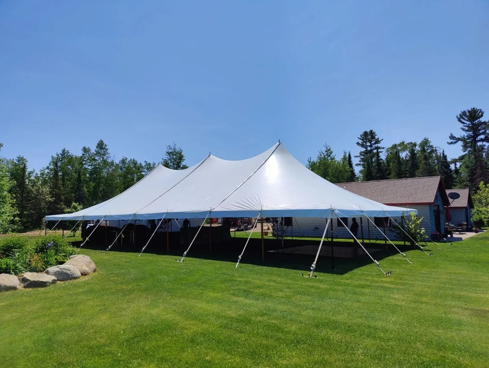 Large white event tent set up on green lawn with trees and a house in the background.