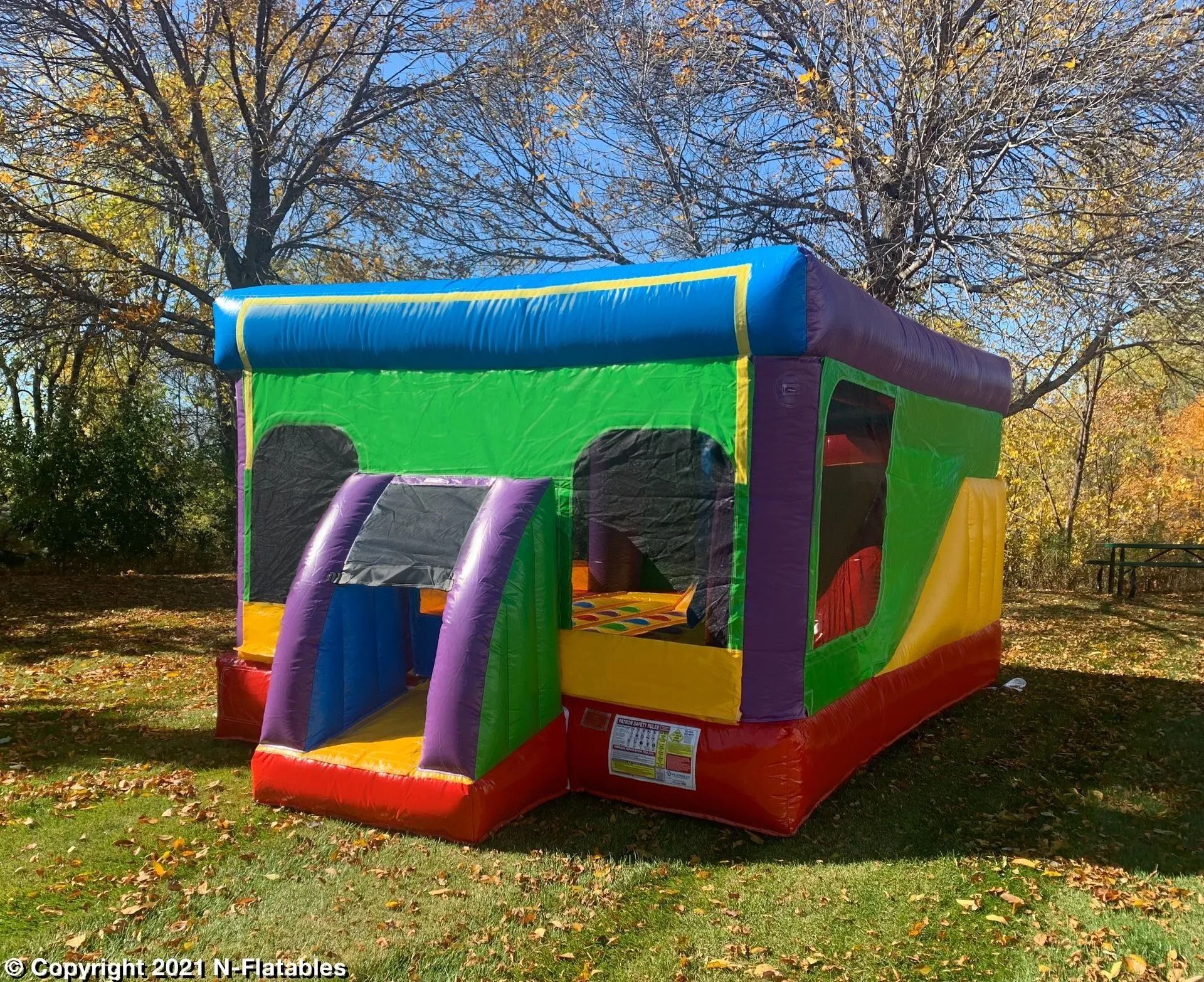 Colorful inflatable bounce house on a grassy lawn with trees in the background under a blue sky.