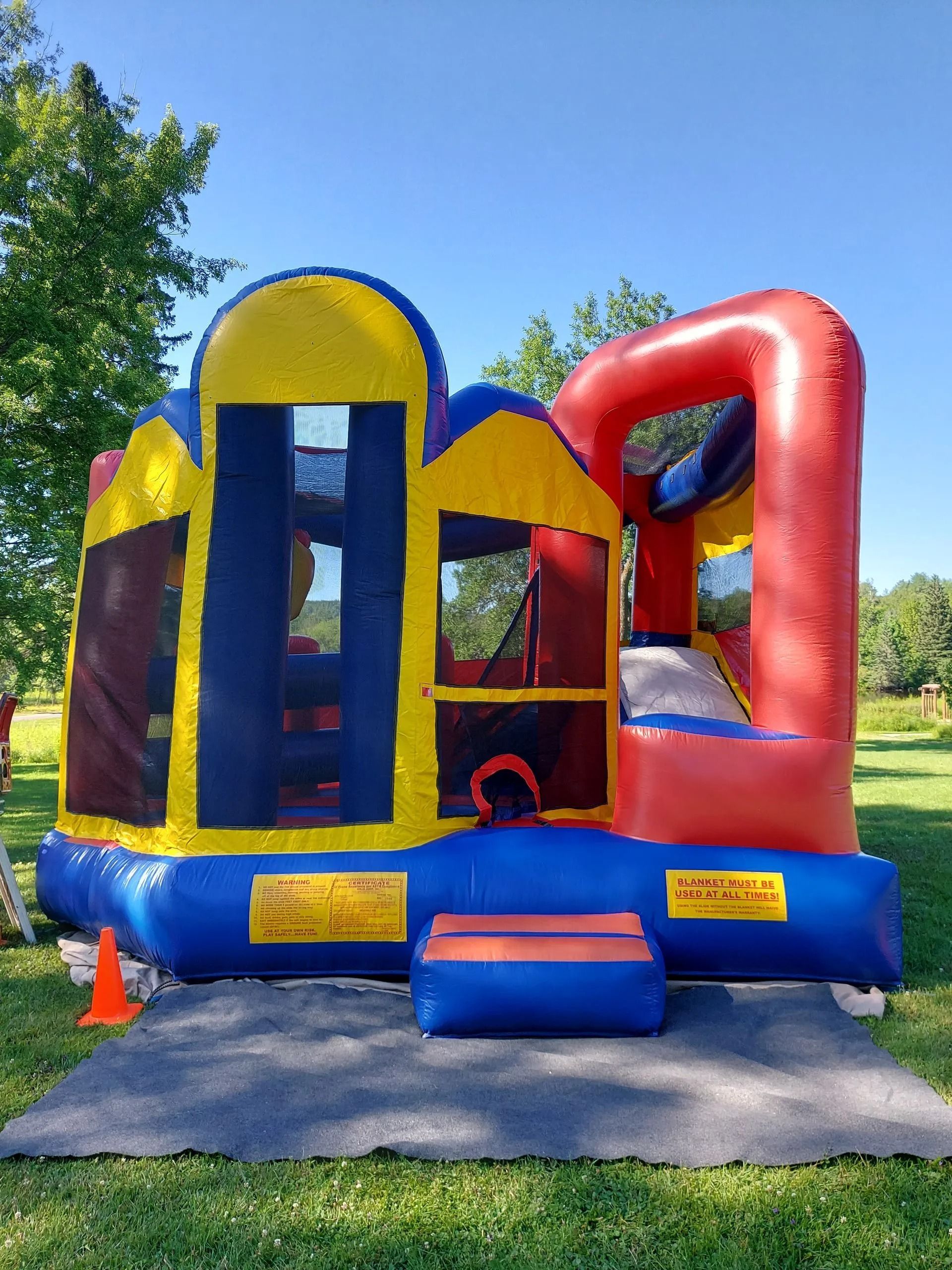 Colorful inflatable bounce house on grass, with a red arch and slide against a blue sky.