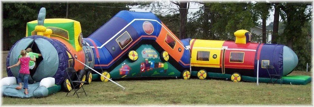 Inflatable train-shaped play structure on grass, with a child entering a tunnel.