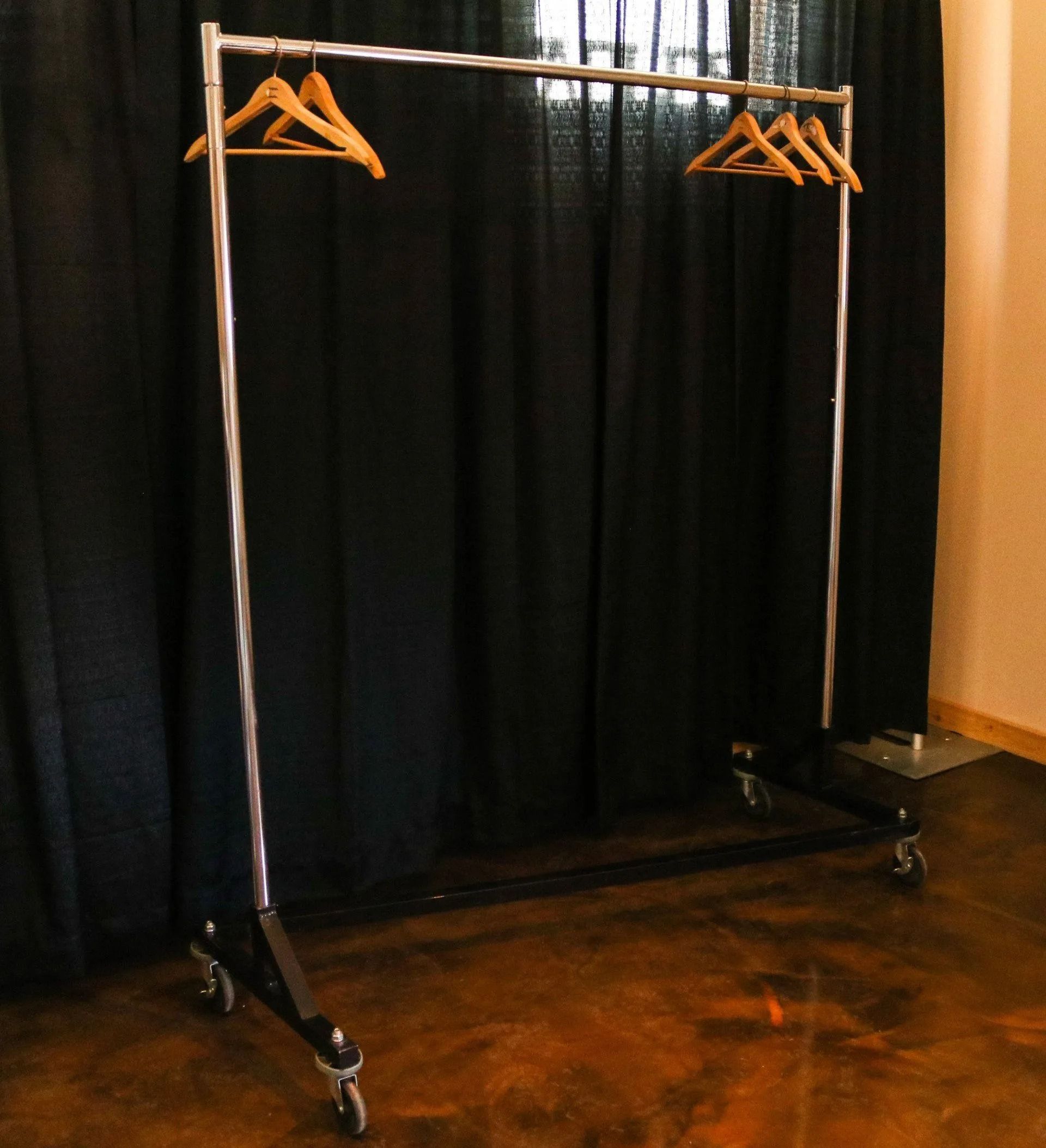 Clothing rack with wooden hangers in front of a black curtain on wheels.