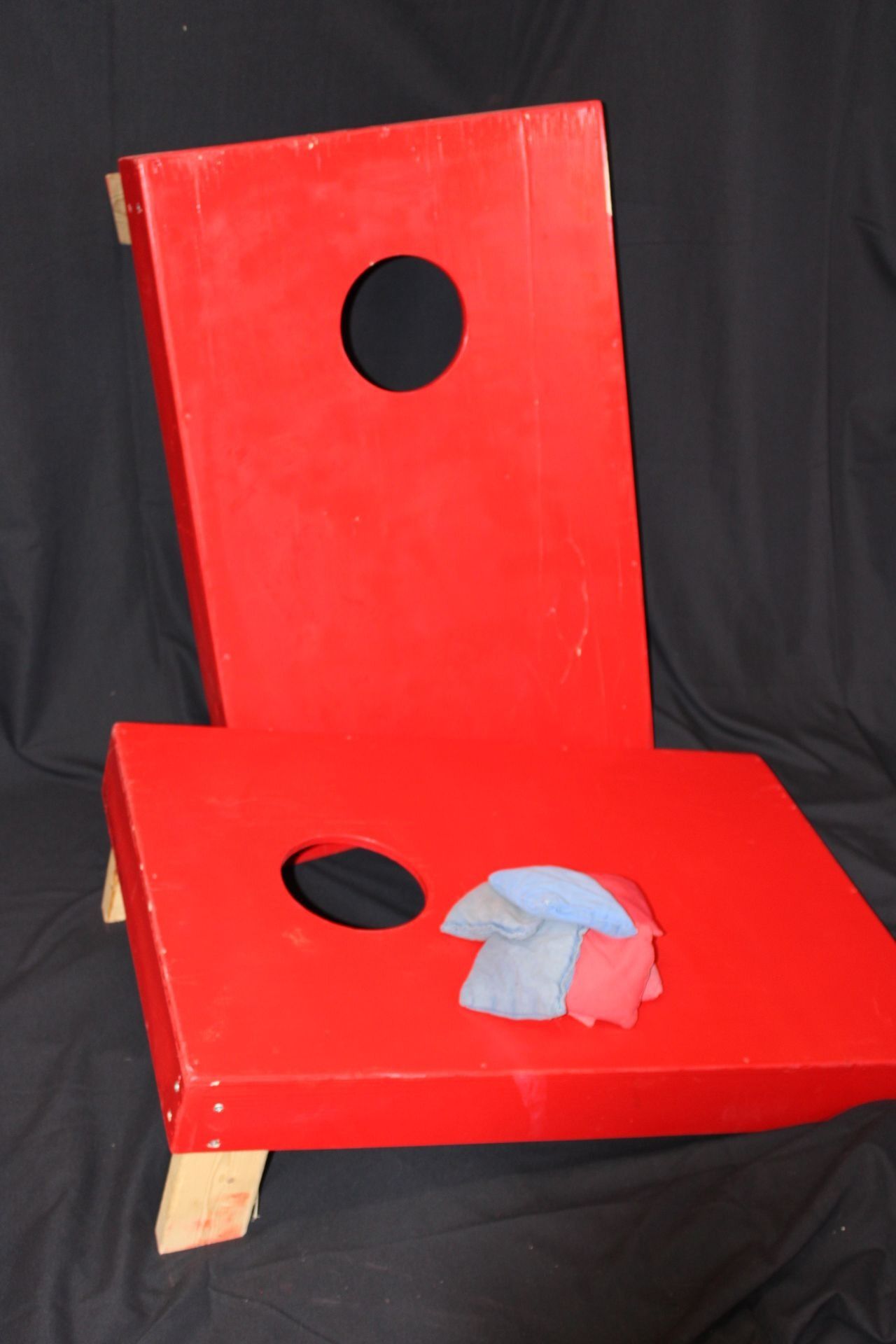 Red cornhole game board with bags on a black background.