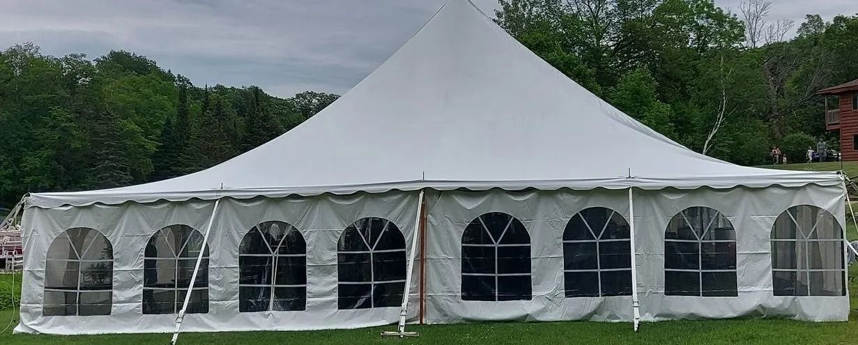 White tent with arched windows set up on grass. Trees in the background.