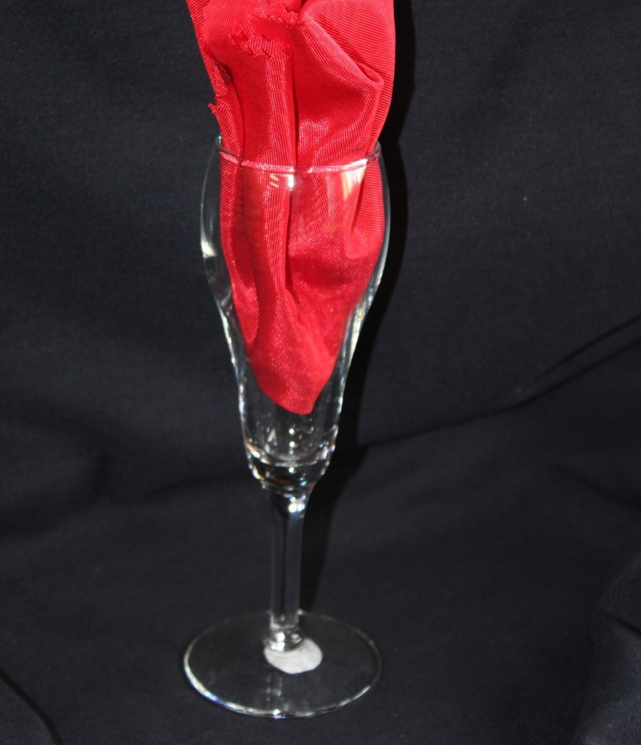 A champagne glass with a folded red napkin inside, on a black background.