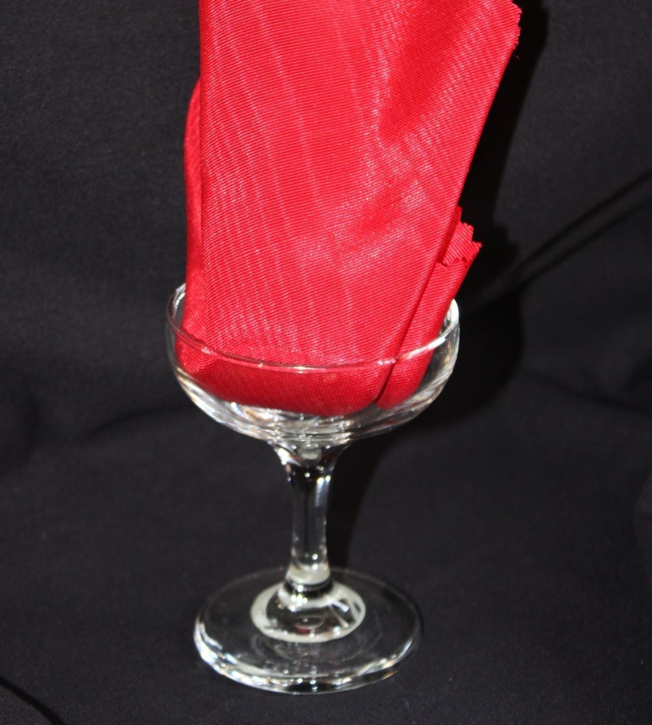 Red napkin in a clear stemmed glass on a black background.