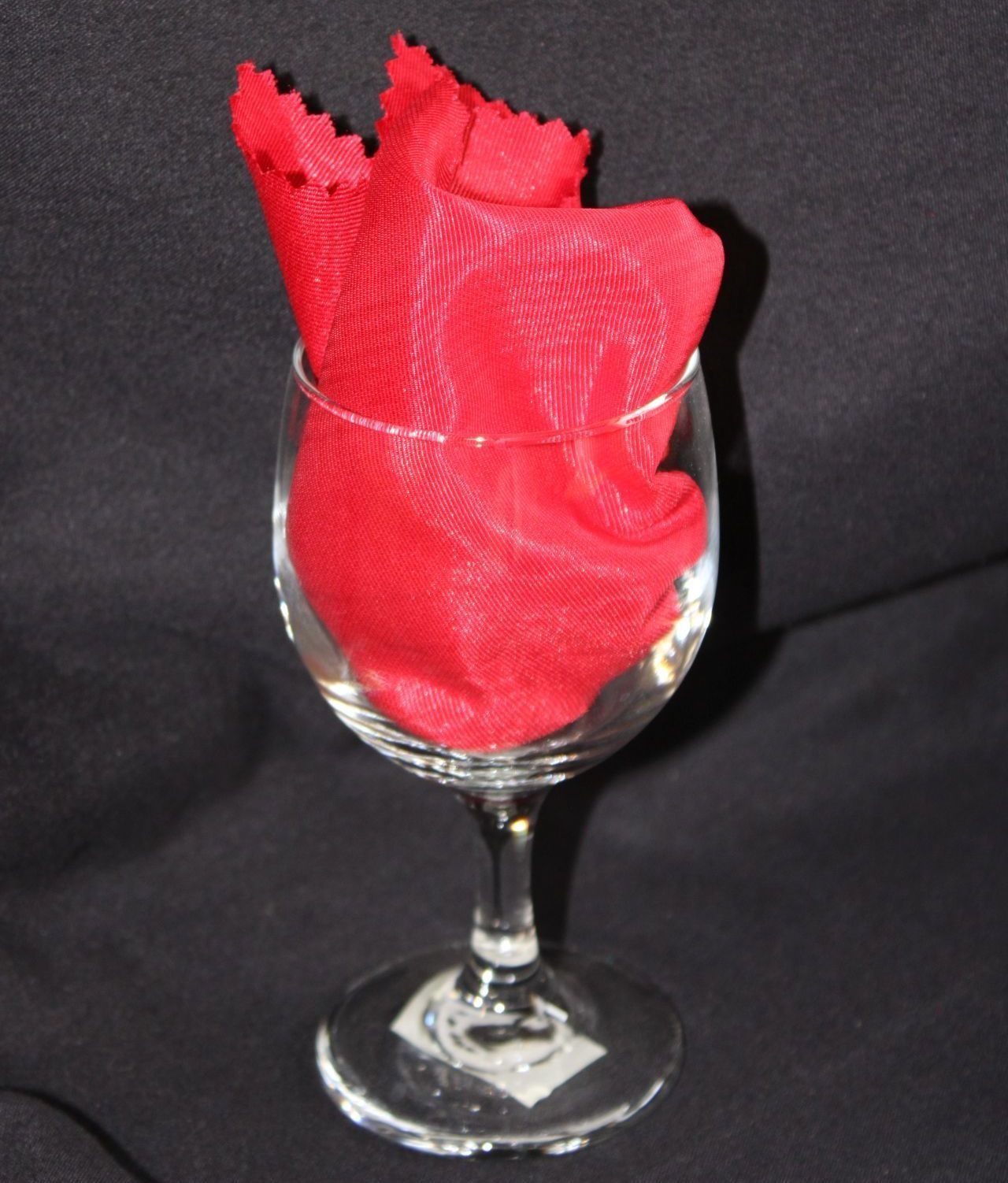 Red napkin arranged in a clear wine glass, on a black background.