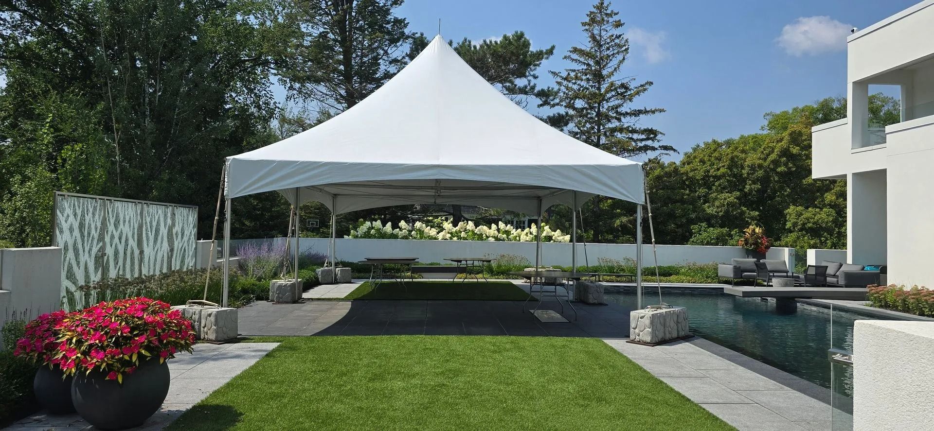 White tent set up on a manicured lawn next to a pool and modern house.