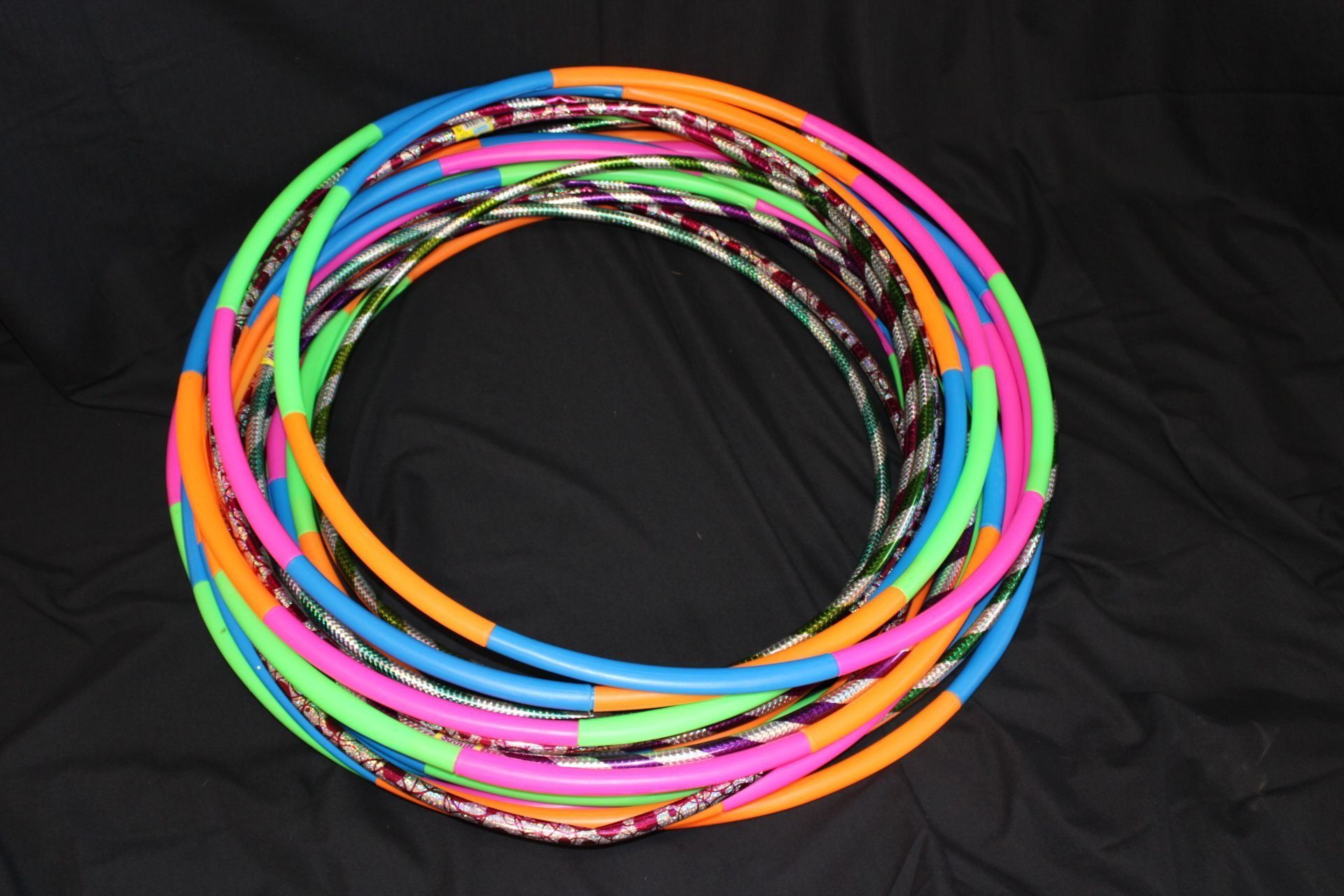 Coiled stack of colorful hula hoops: pink, orange, green, blue, and patterned silver.