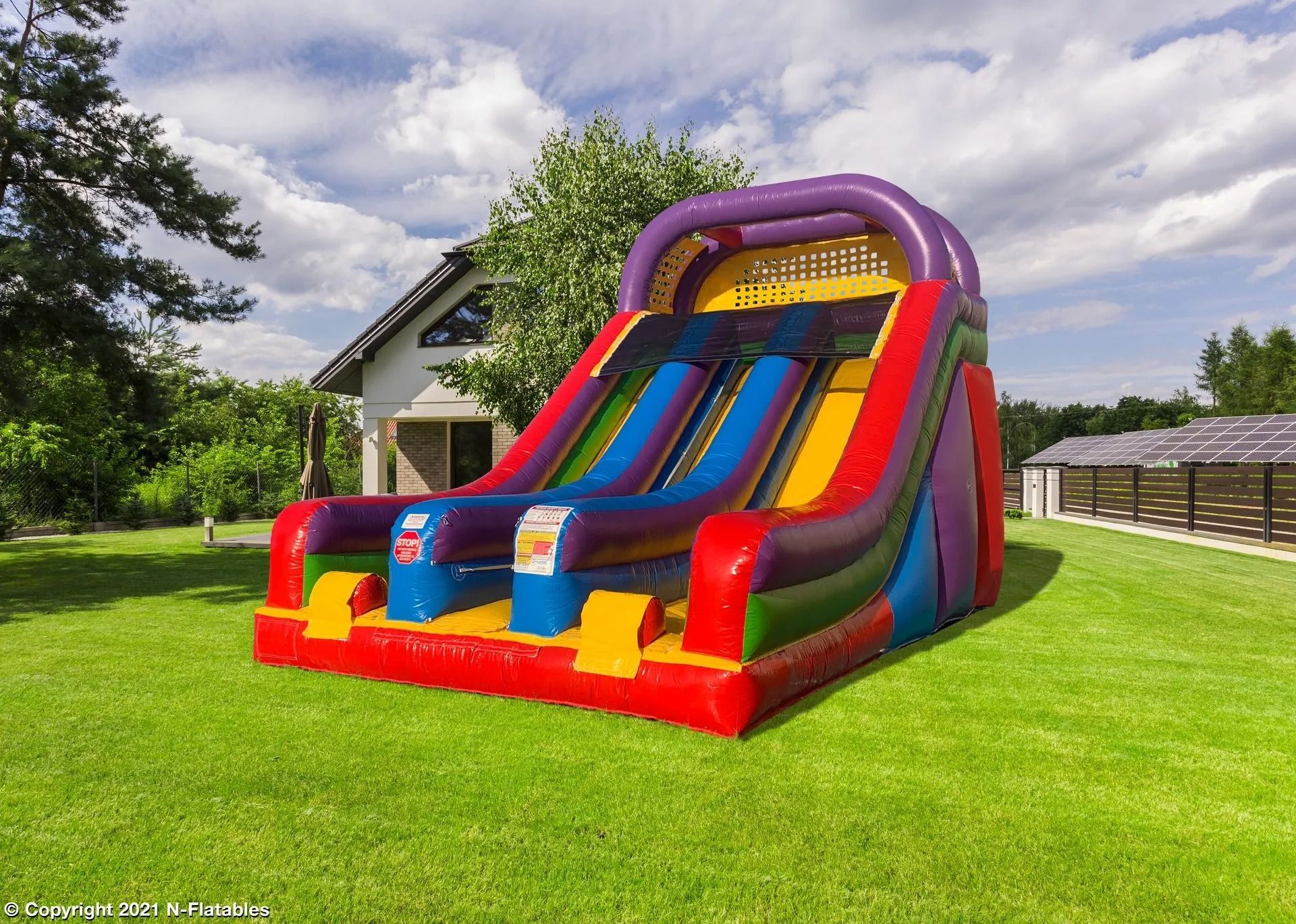 A large, multi-colored inflatable slide on a grassy lawn in front of a house.