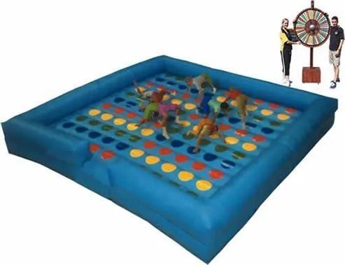 Giant inflatable Twister game with people playing, colorful spots, blue base, and a steering wheel spinner.