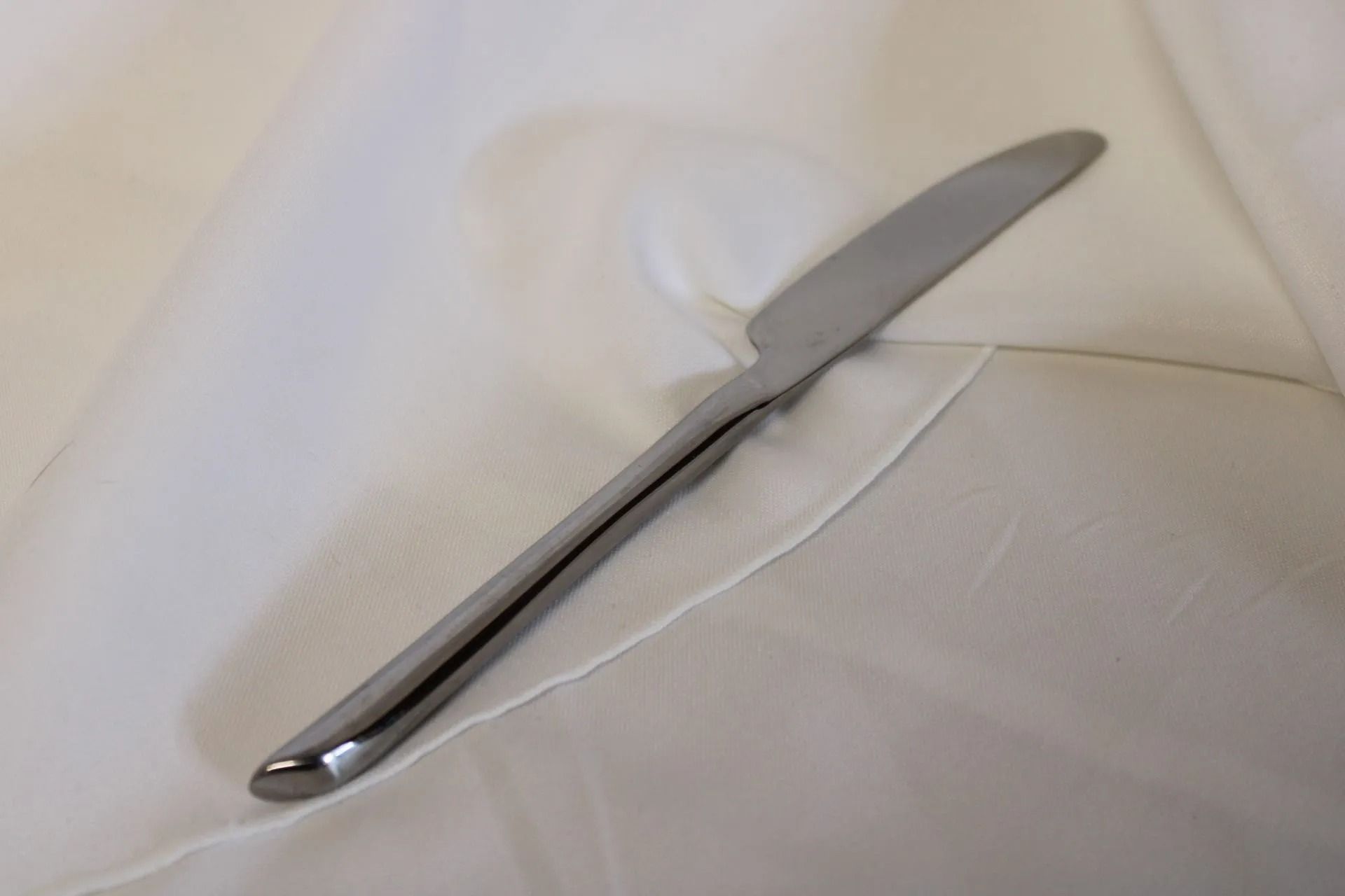 Silver dinner knife resting on a white tablecloth.