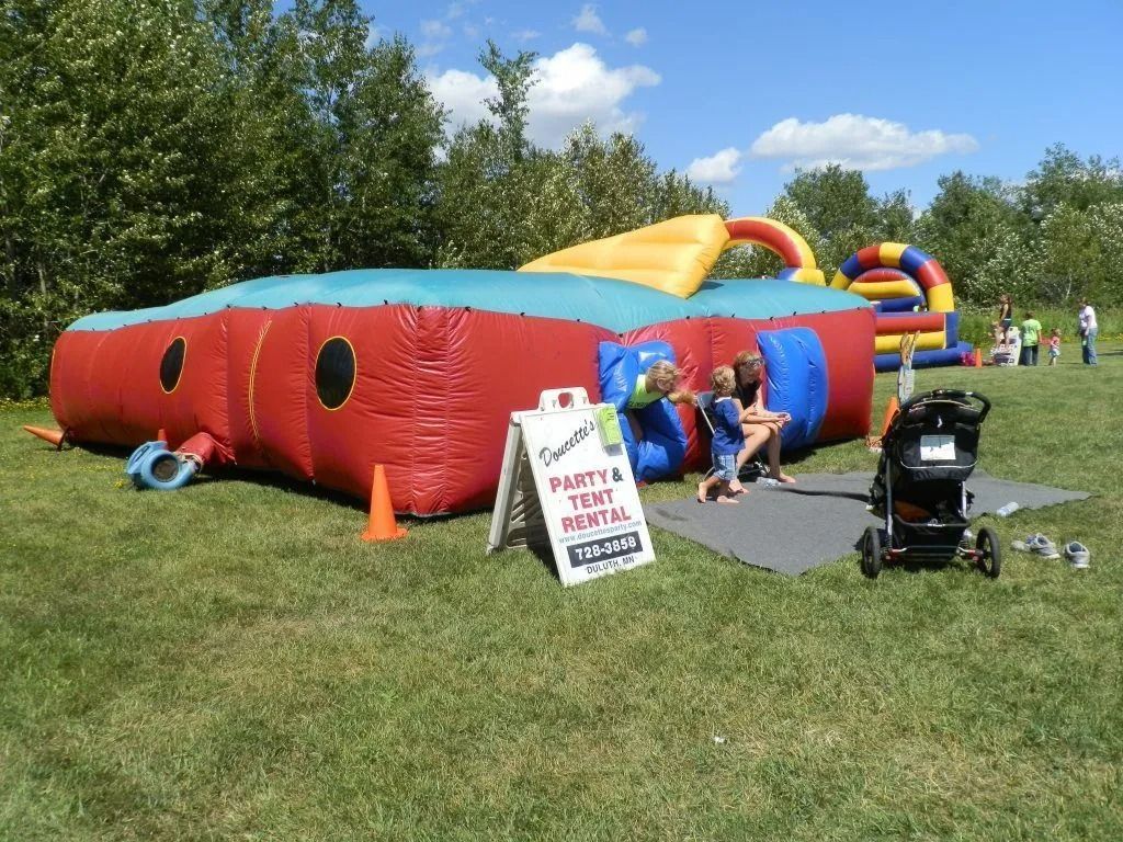 Inflatable bounce house at an outdoor party with children, stroller, and sign.
