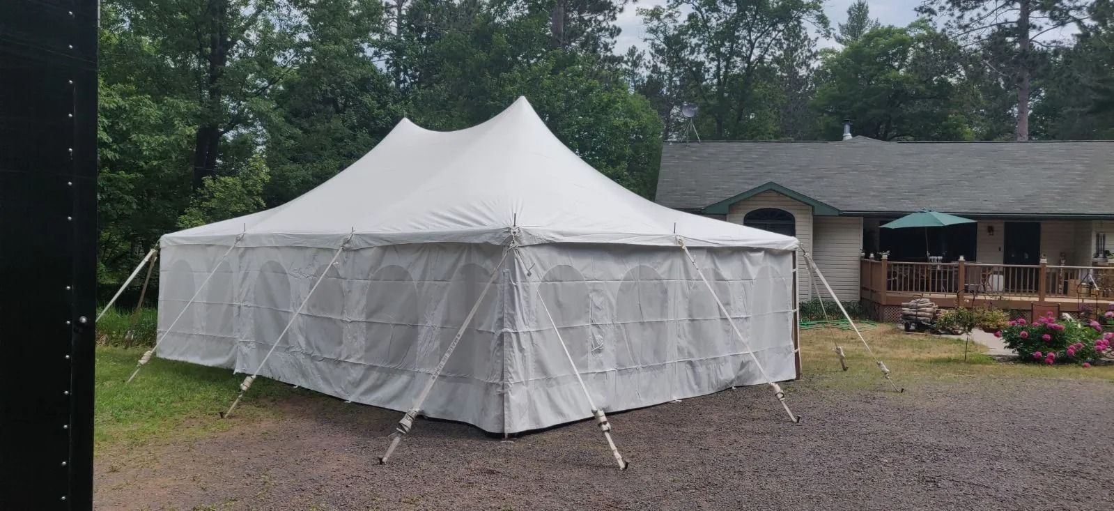 White tent set up on gravel, with a house and trees in the background.
