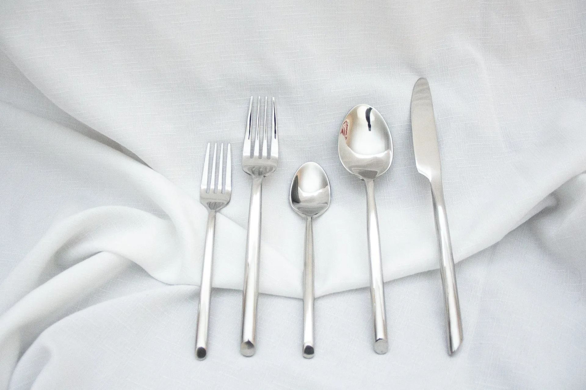 Silver flatware on white fabric: fork, salad fork, spoon, teaspoon, and knife.
