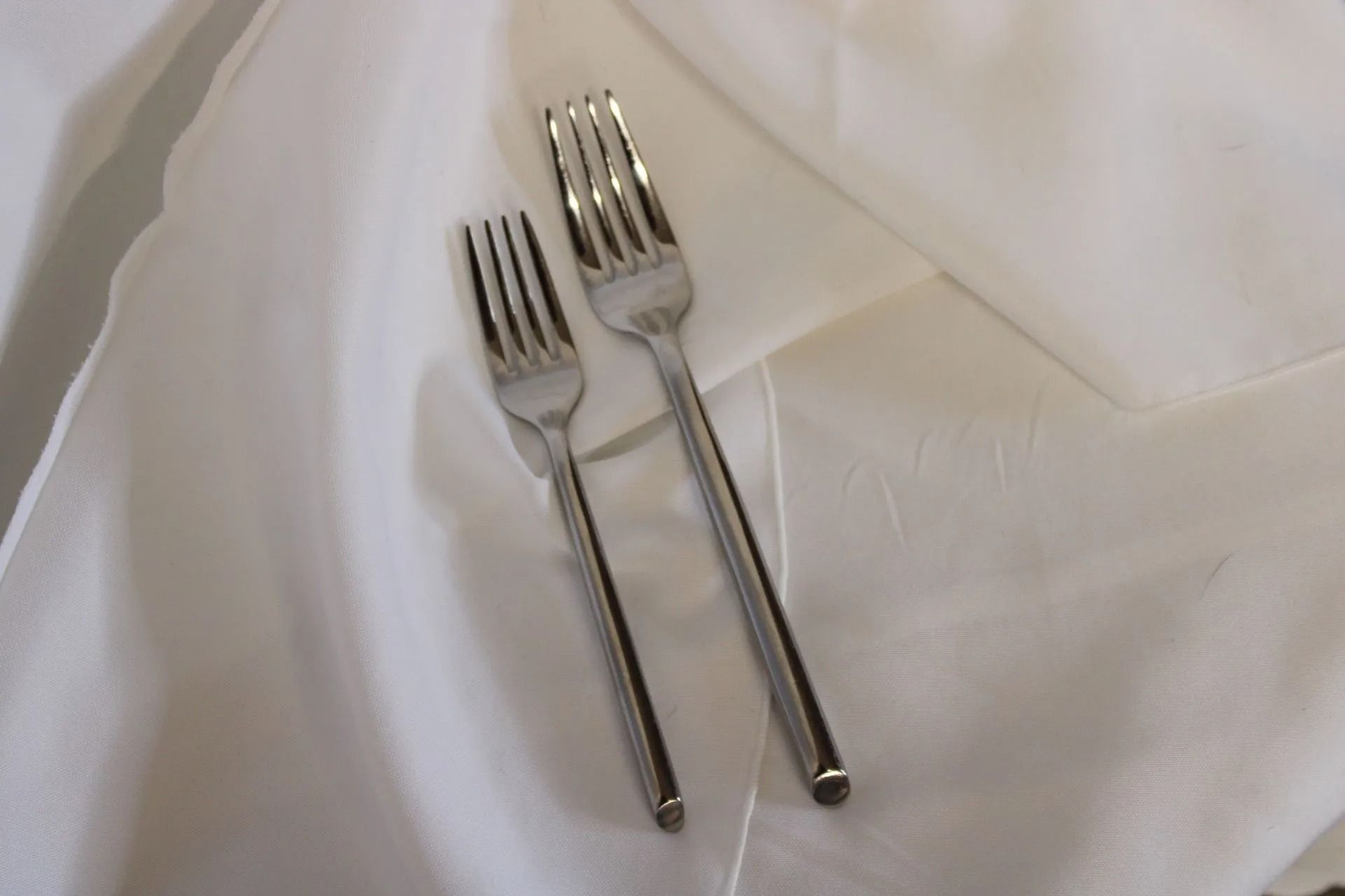 Two silver forks on a white cloth.