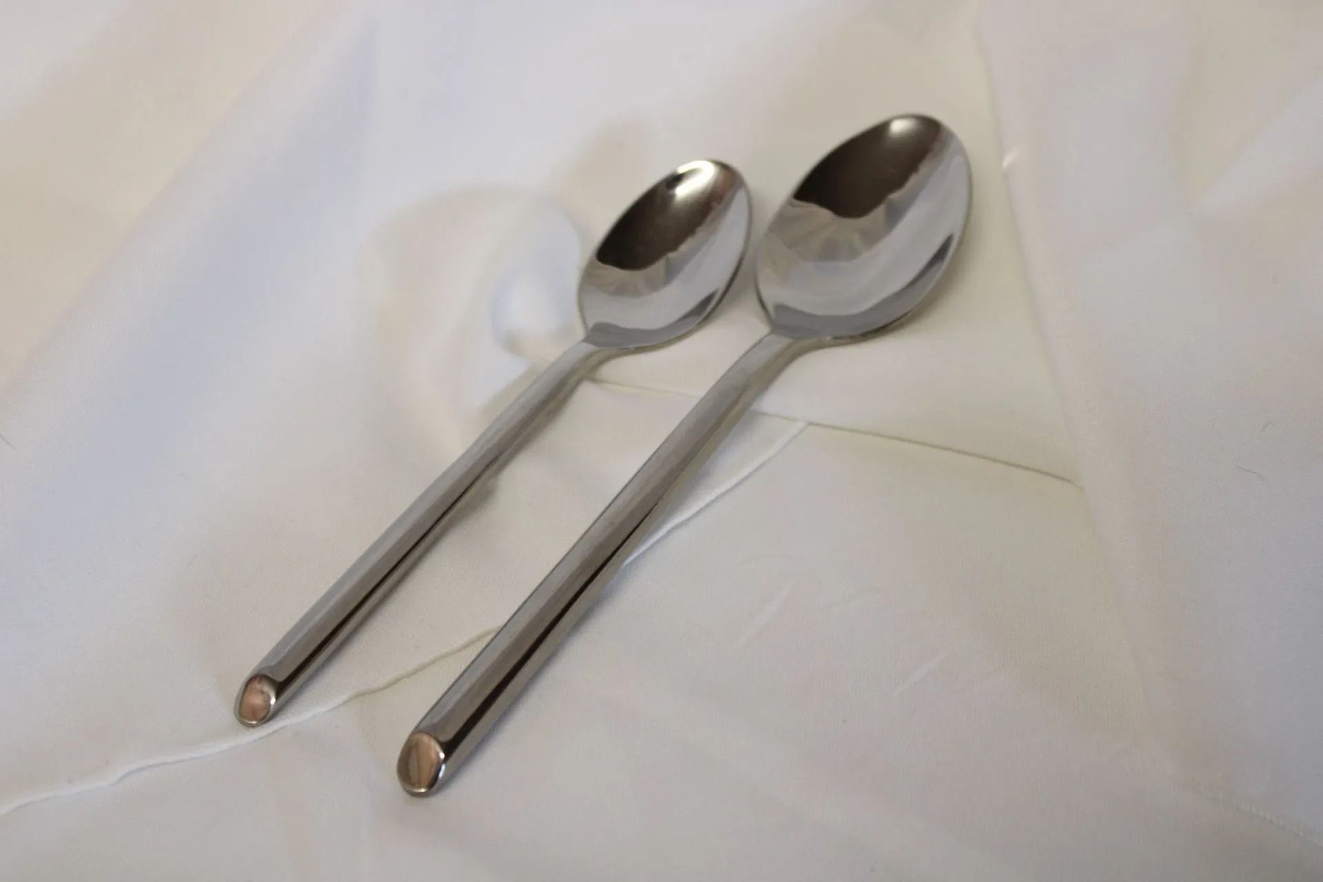 Two shiny silver spoons on white fabric.