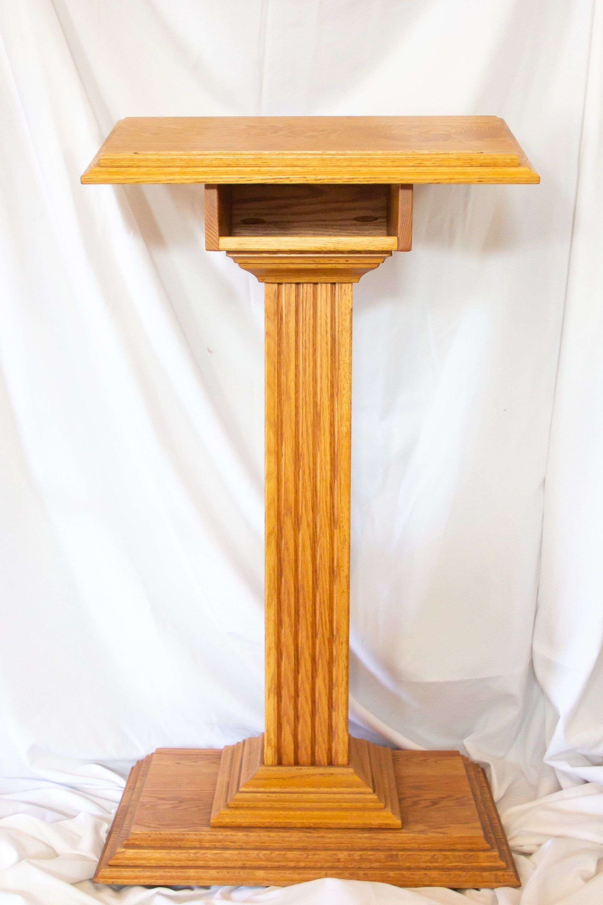 Wooden podium with fluted pillar, a reading surface, and a base. Light brown.