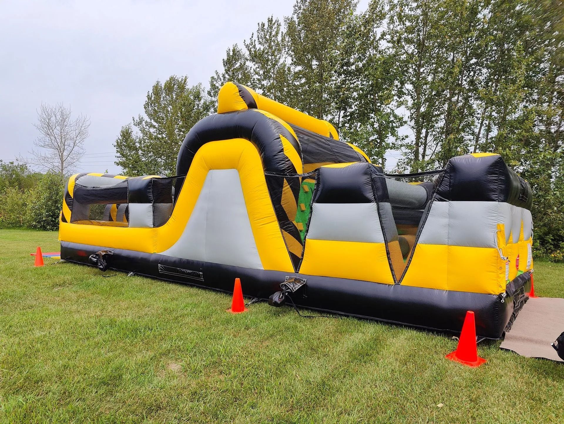 Inflatable obstacle course, yellow and black with grey accents, set on grass with orange cones.