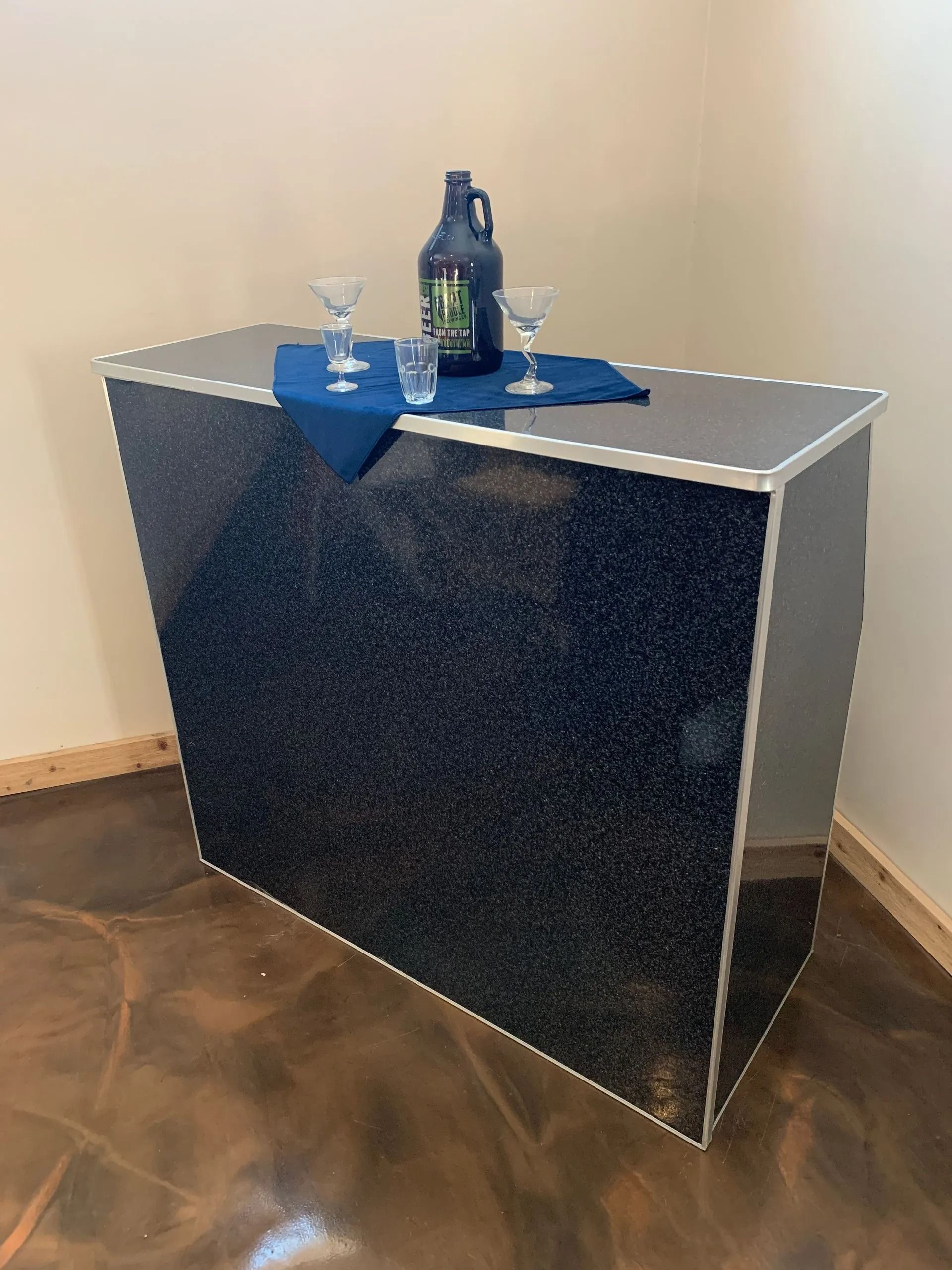 Black glitter bar with silver trim, blue napkin, and drinks on top.