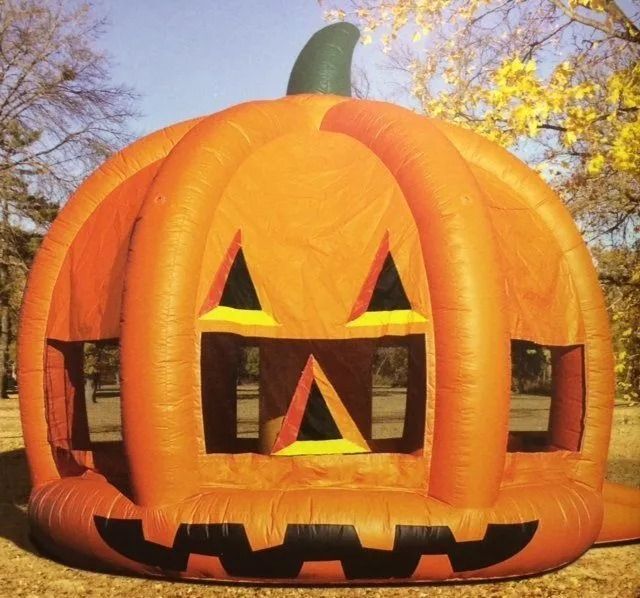 Orange inflatable pumpkin bounce house with carved face and windows, outdoors.