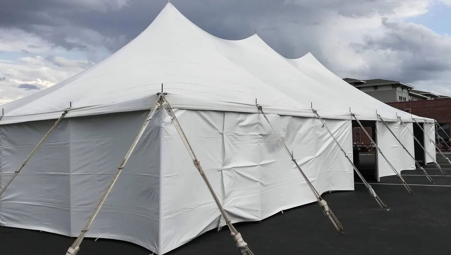 White tent set up outdoors, supported by poles. Cloudy sky in the background.
