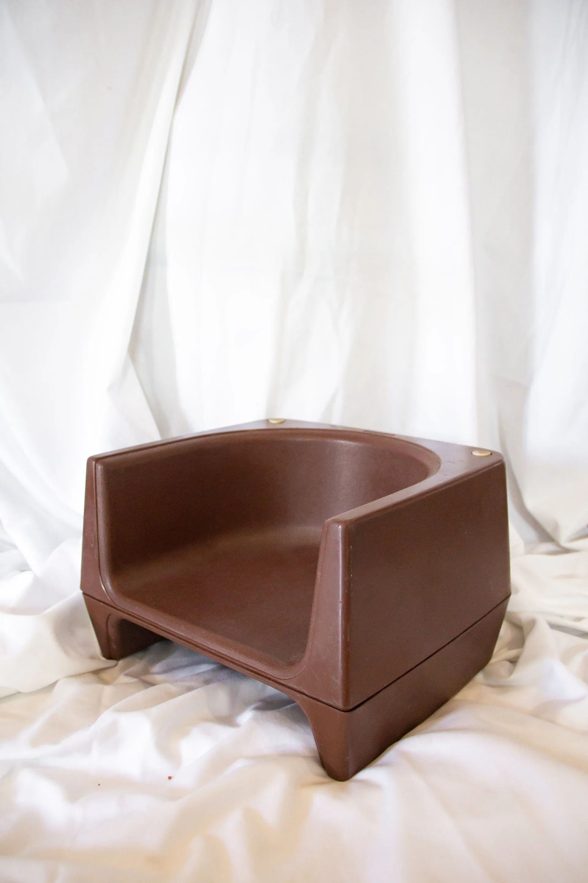 Brown plastic child's chair with a rounded back, on a white cloth backdrop.