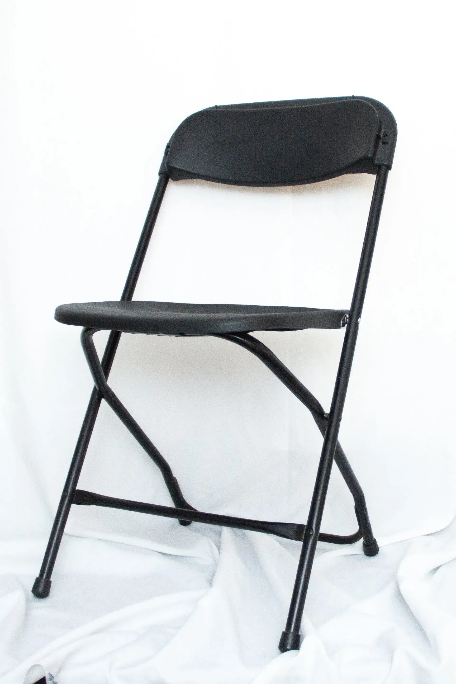 Black folding chair on a white surface, shown from the front.