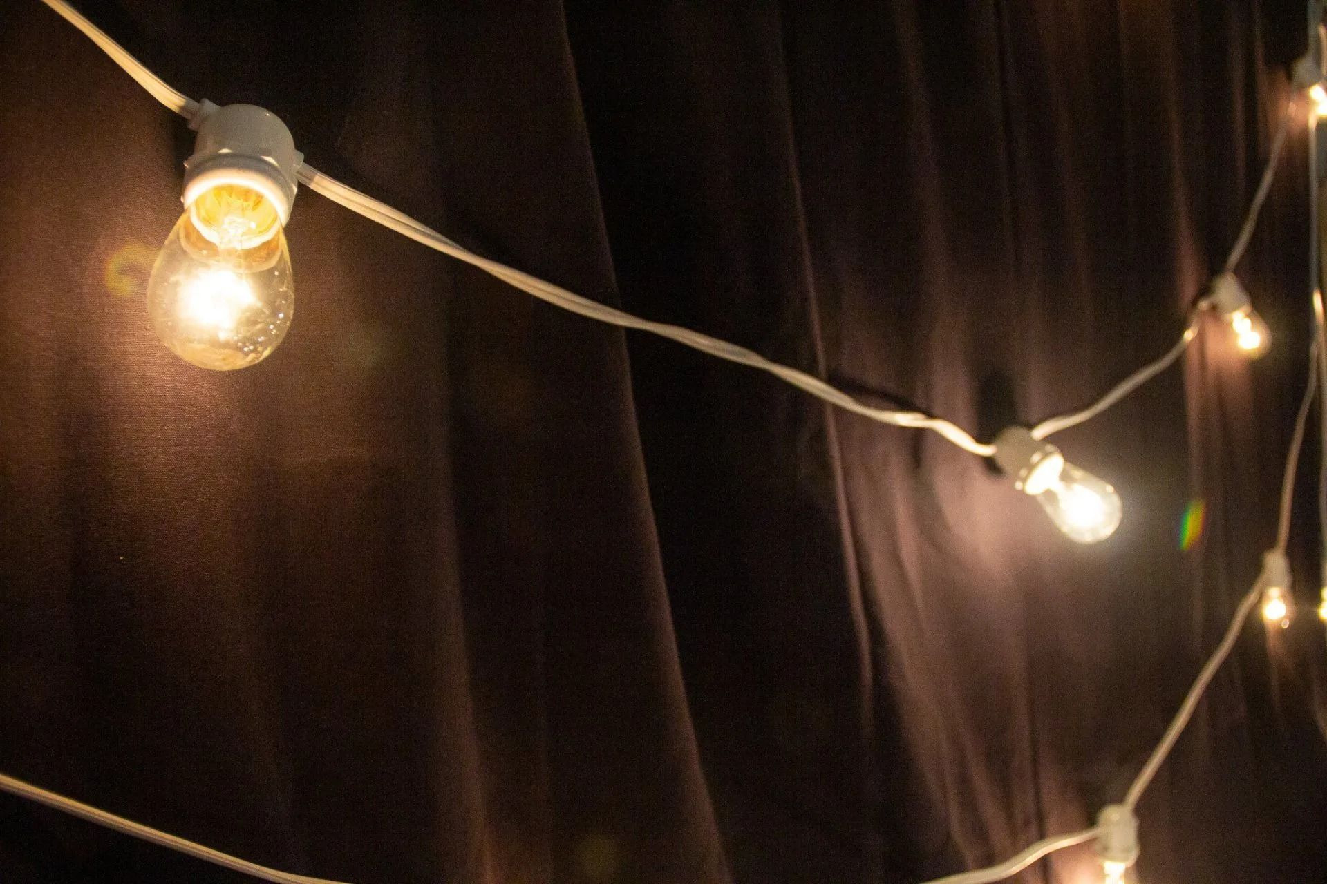String lights illuminate a dark, brown curtain.