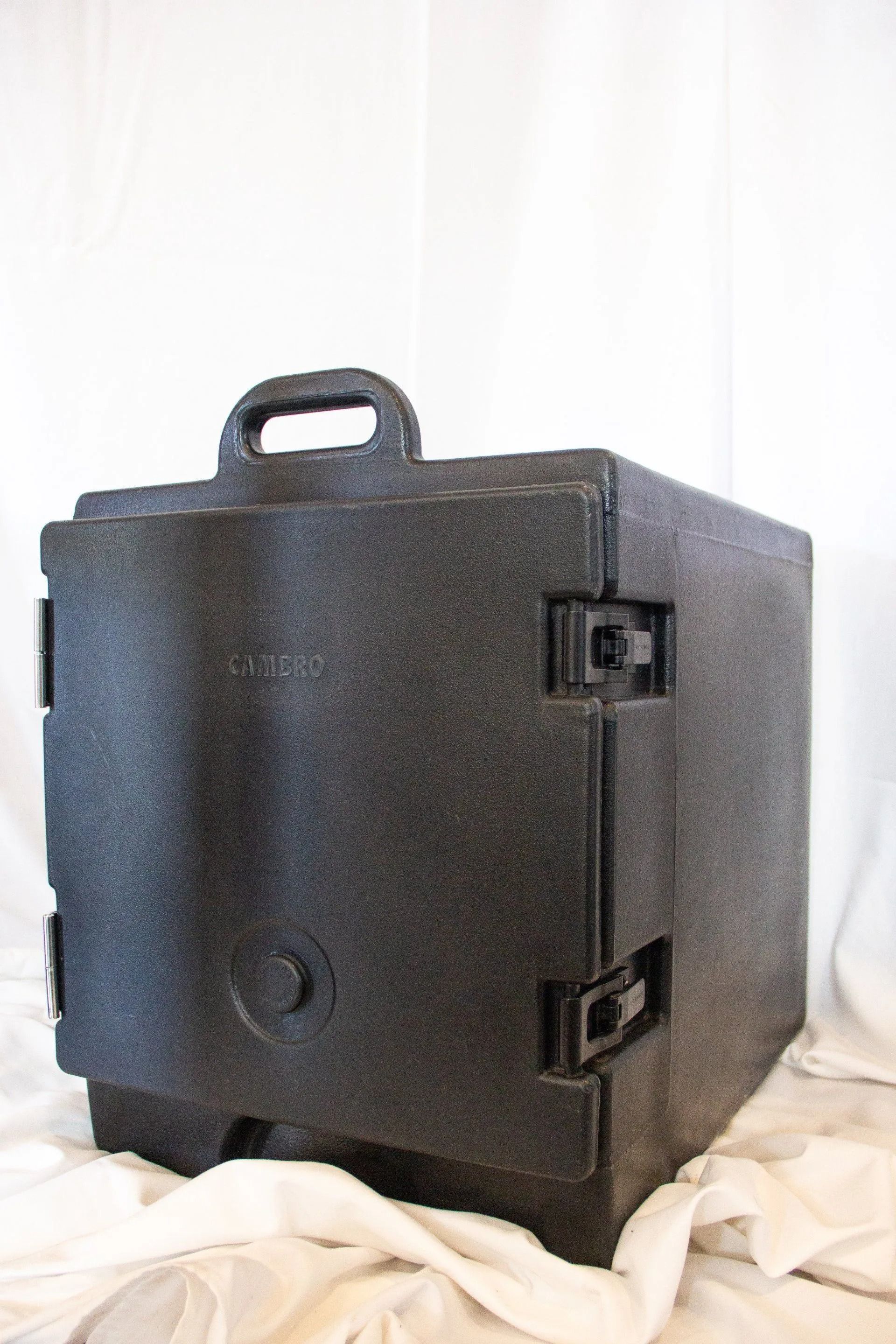 Black insulated food carrier with handle and latches, sitting on white cloth.