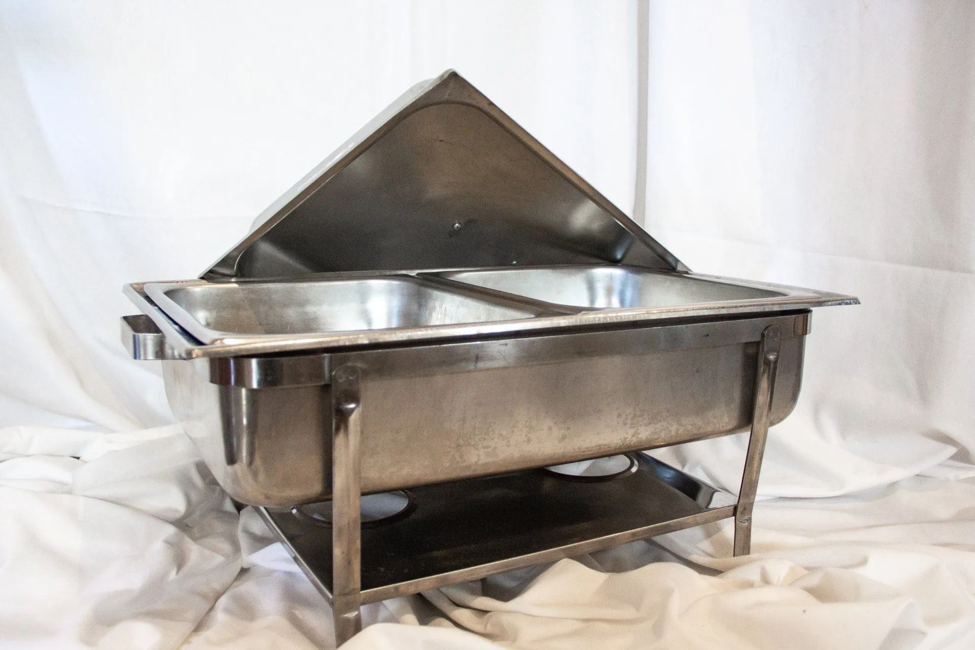 Stainless steel chafing dish with lid open on a white cloth.