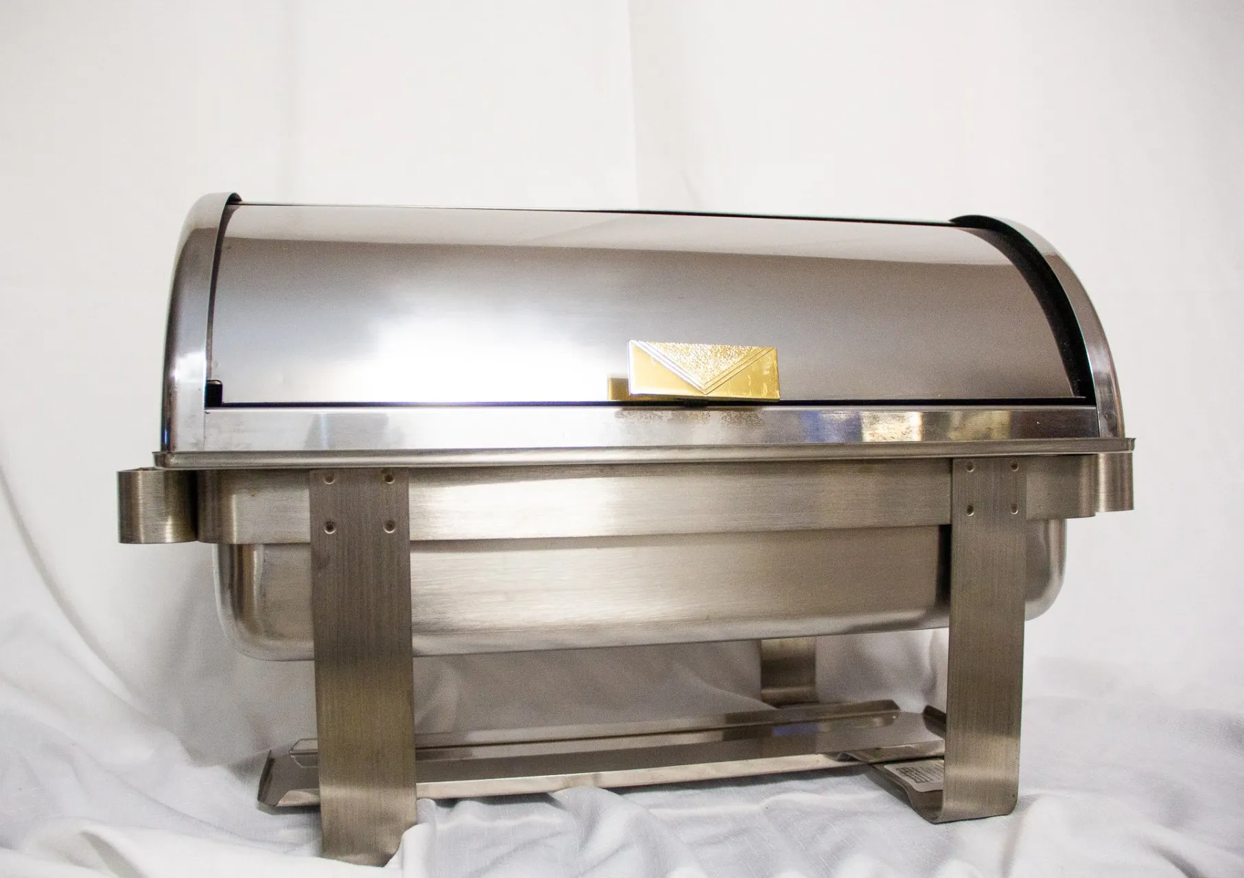 Stainless steel chafing dish with lid open slightly, on a white surface.