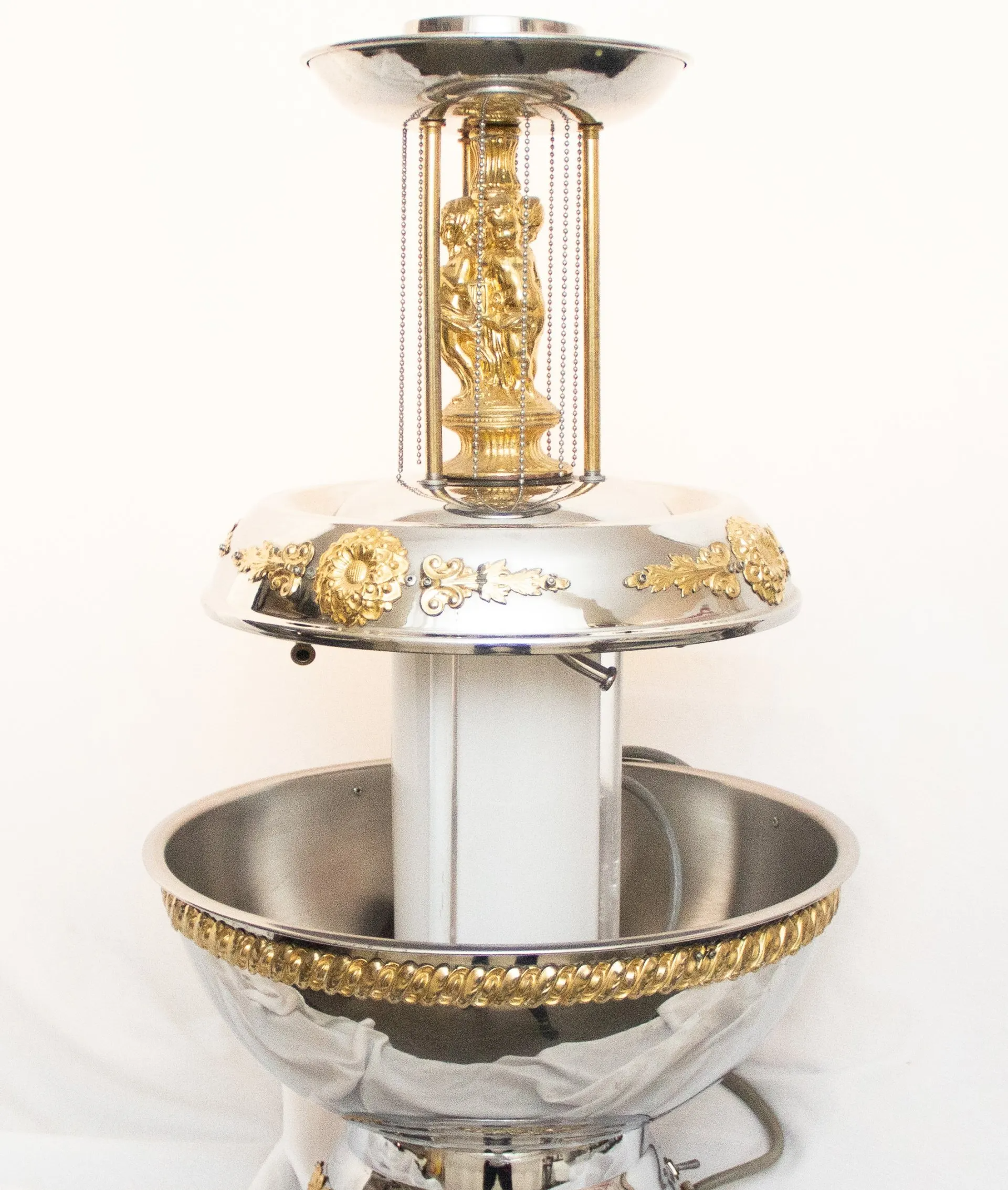 Silver and gold tiered fountain with a central column, decorative accents, and a small sculpture inside.