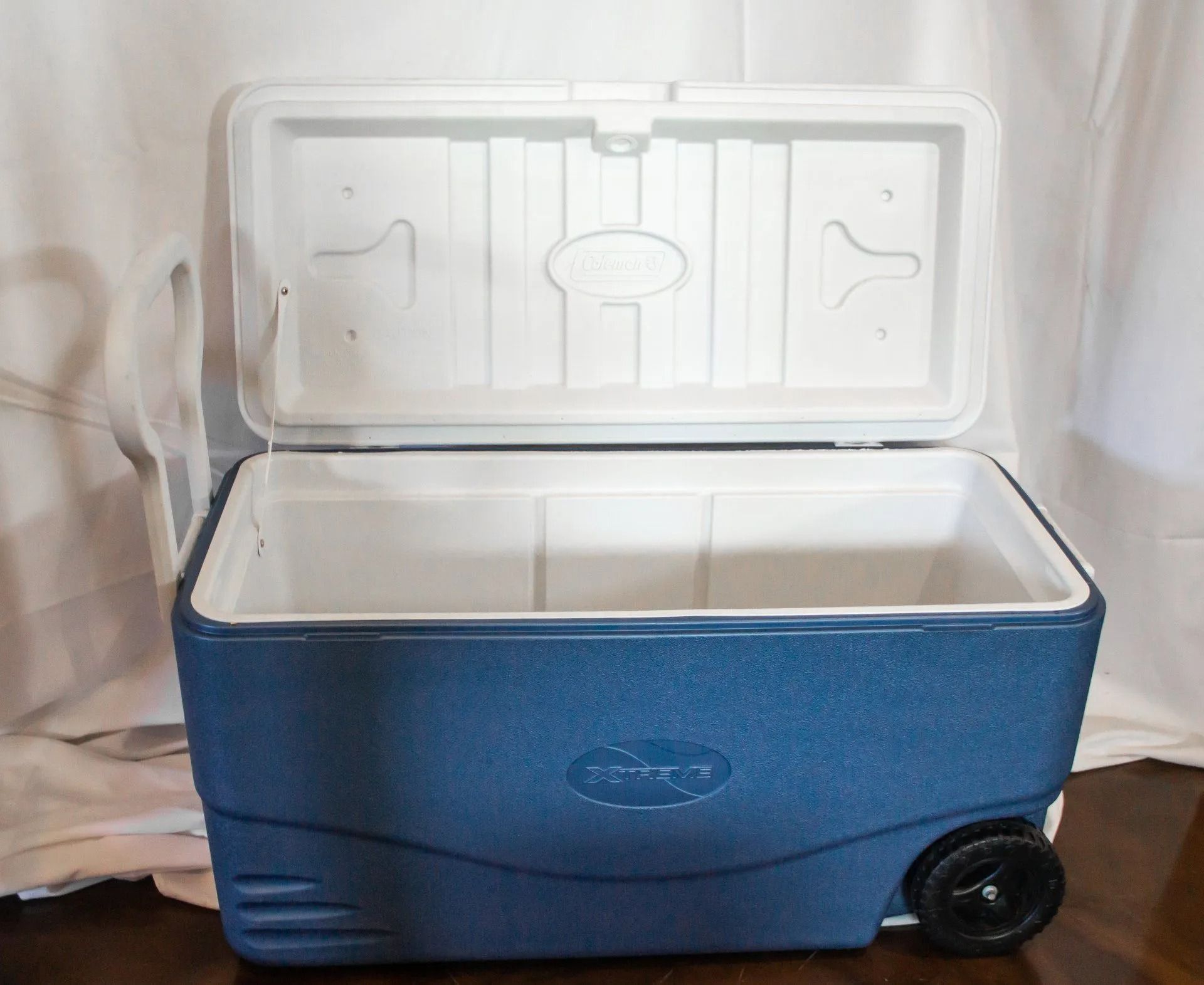 Blue cooler with white interior, lid open, black wheel visible on the side.