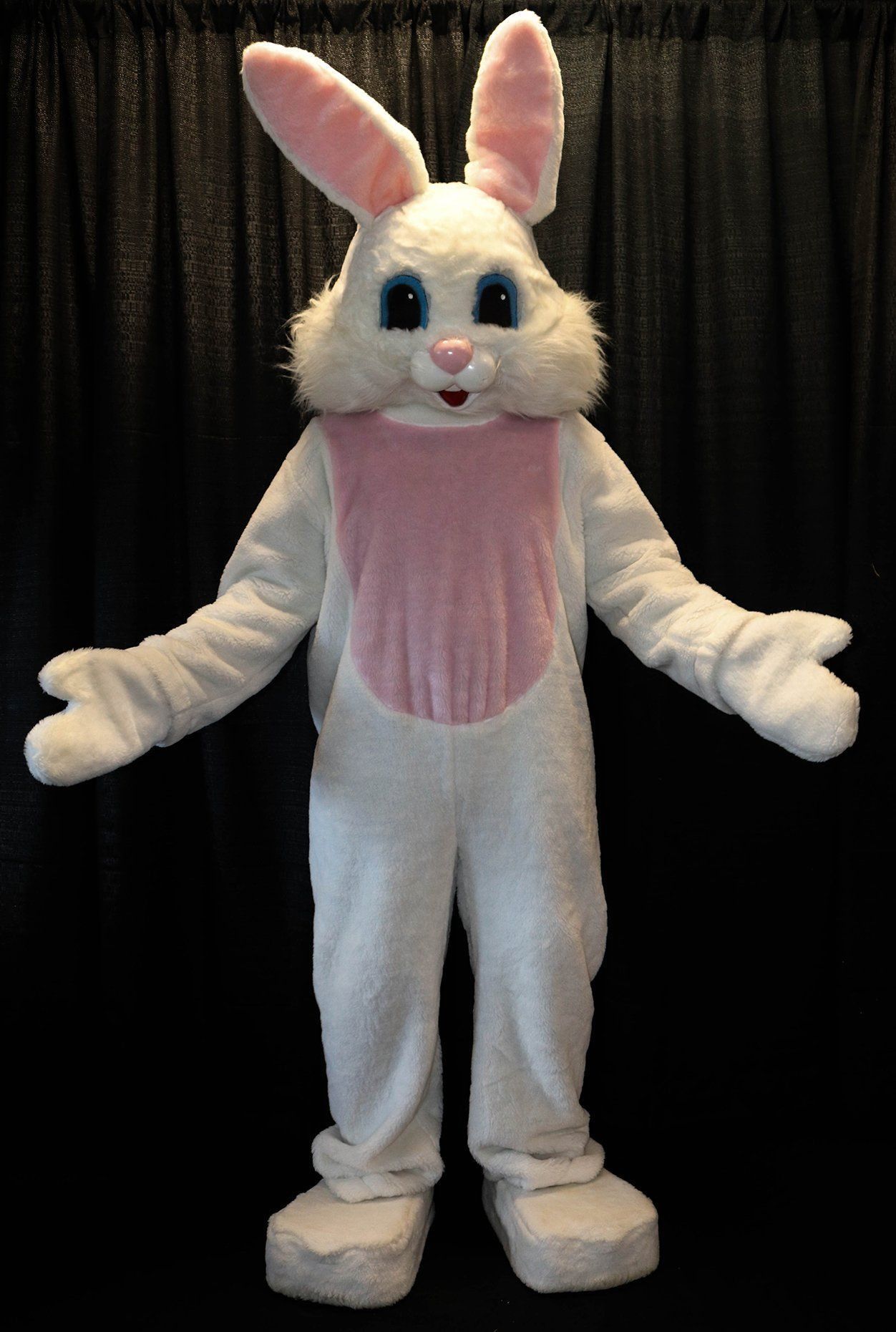 White Easter Bunny mascot with arms outstretched, black backdrop.